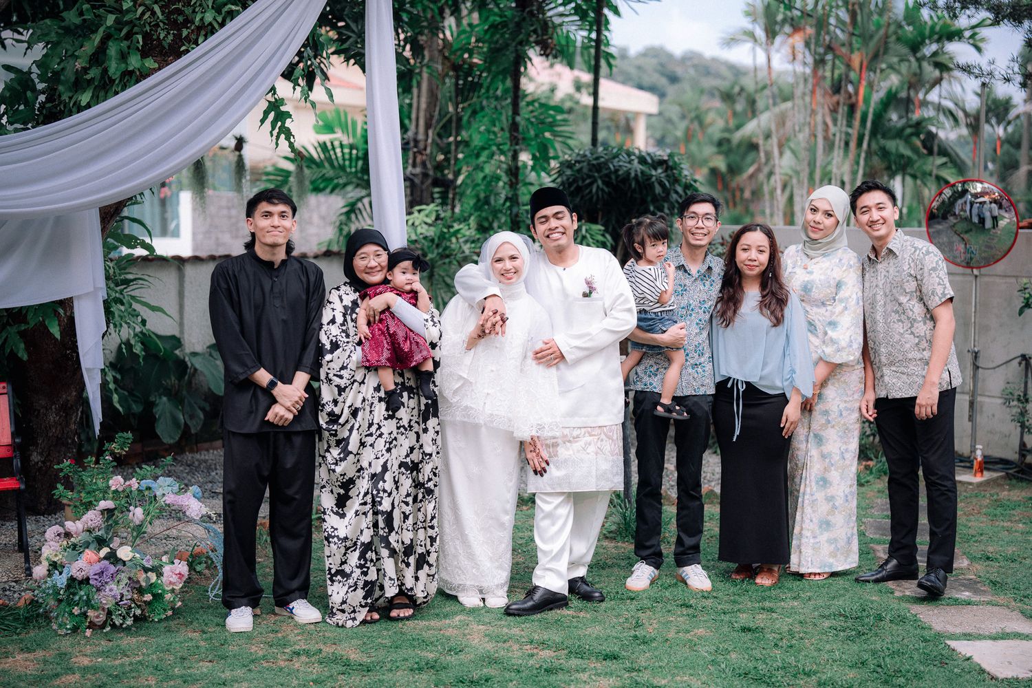 Group of elegantly dressed family members posing together at an outdoor wedding celebration on a green lawn.
