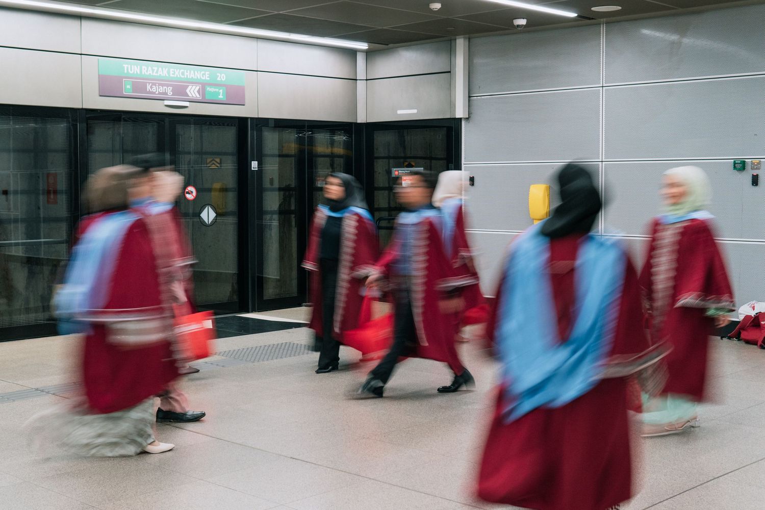 Blurred motion of people walking in red graduation robes through a modern hallway.