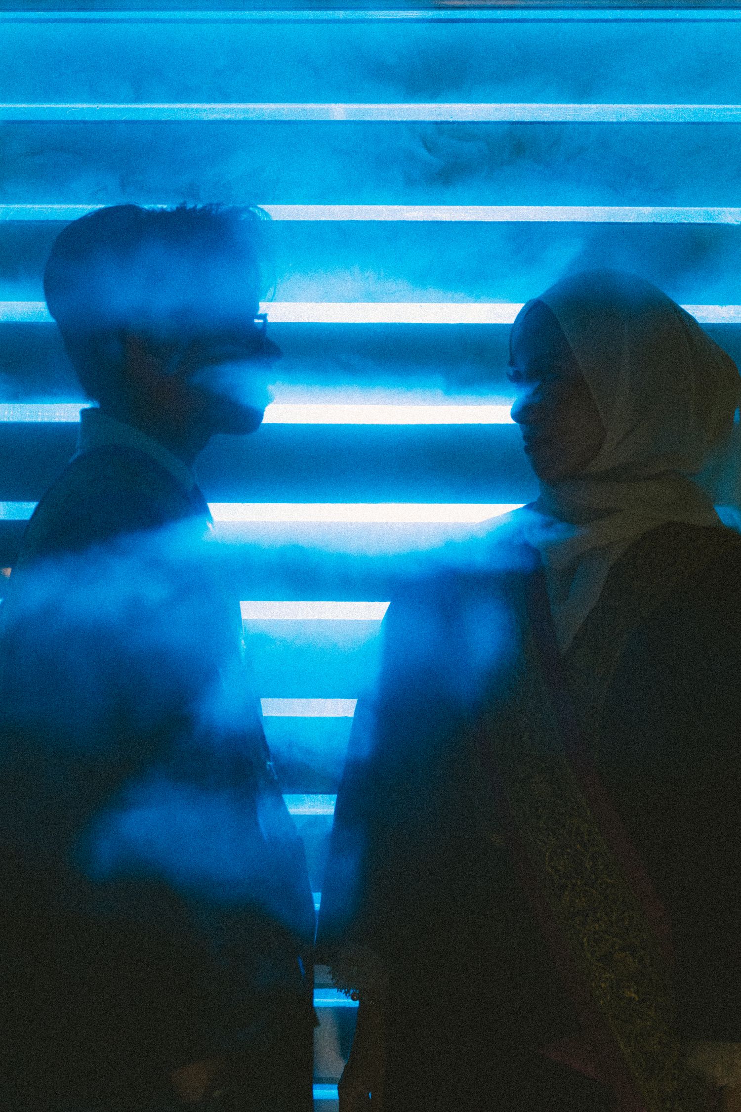 Silhouettes against blue neon lighting in a corridor create a moody atmosphere.