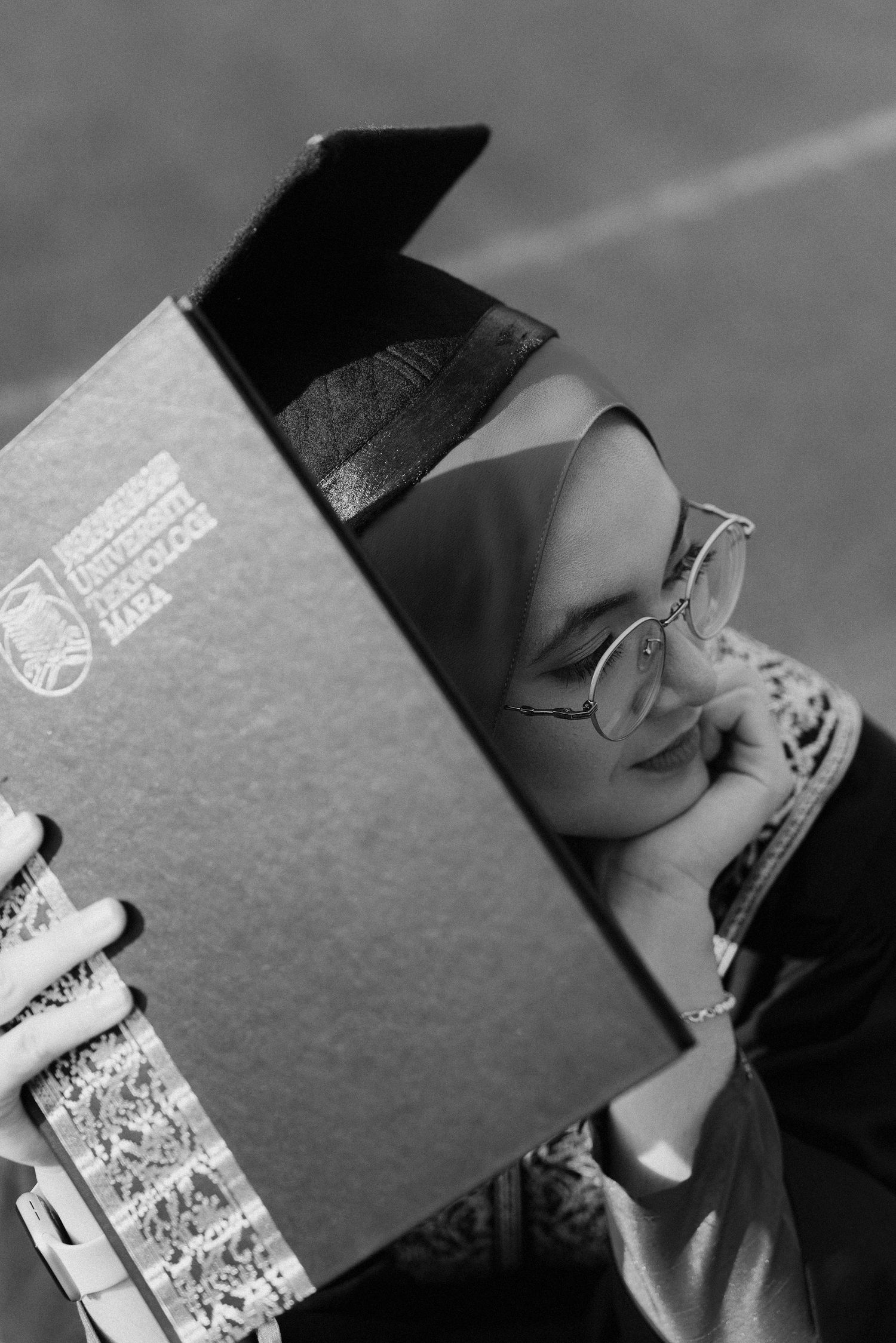Person peeking behind a book while wearing glasses in a black and white photograph.
