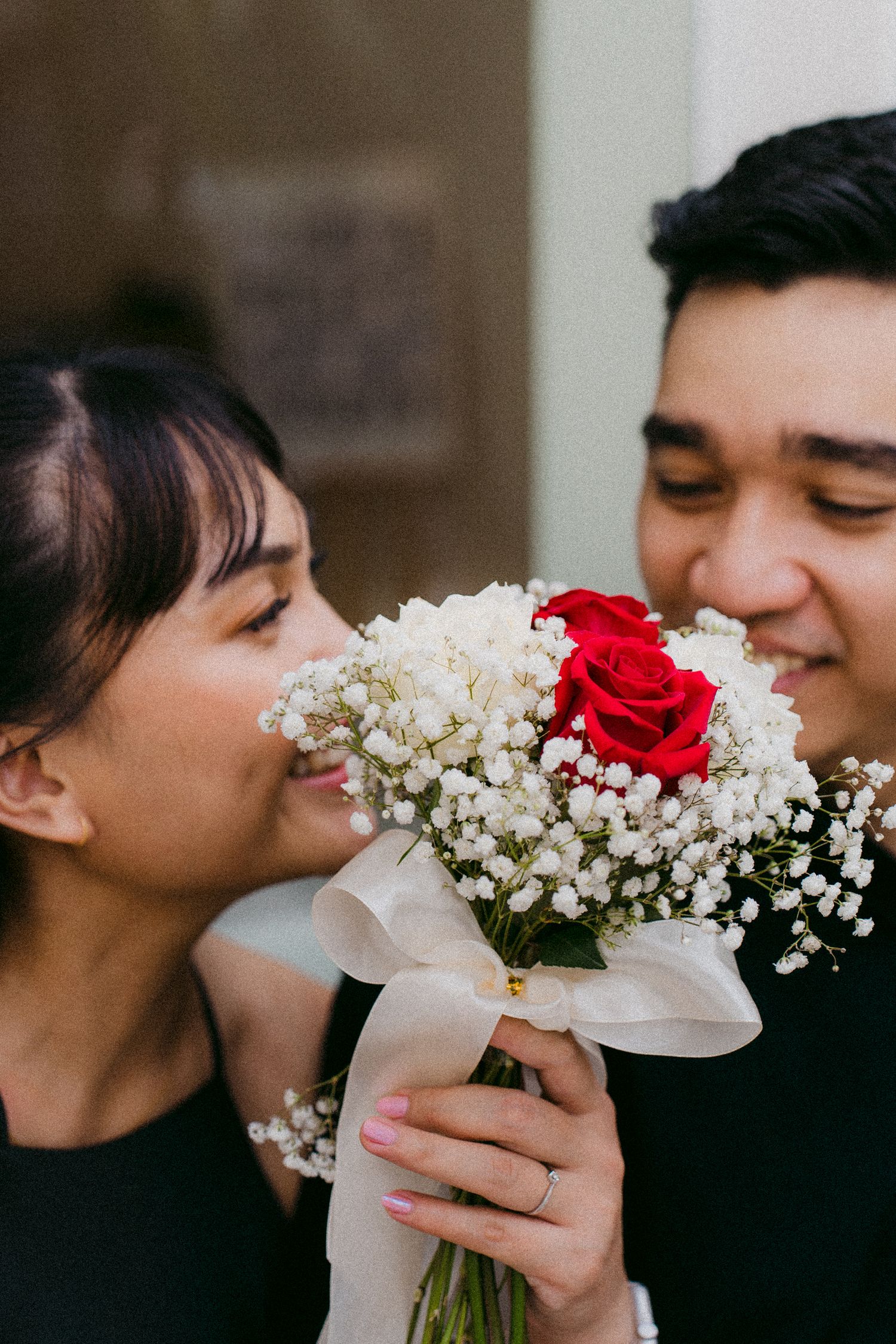 A couple sharing an intimate moment while holding a bouquet of red roses and baby's breath flowers.