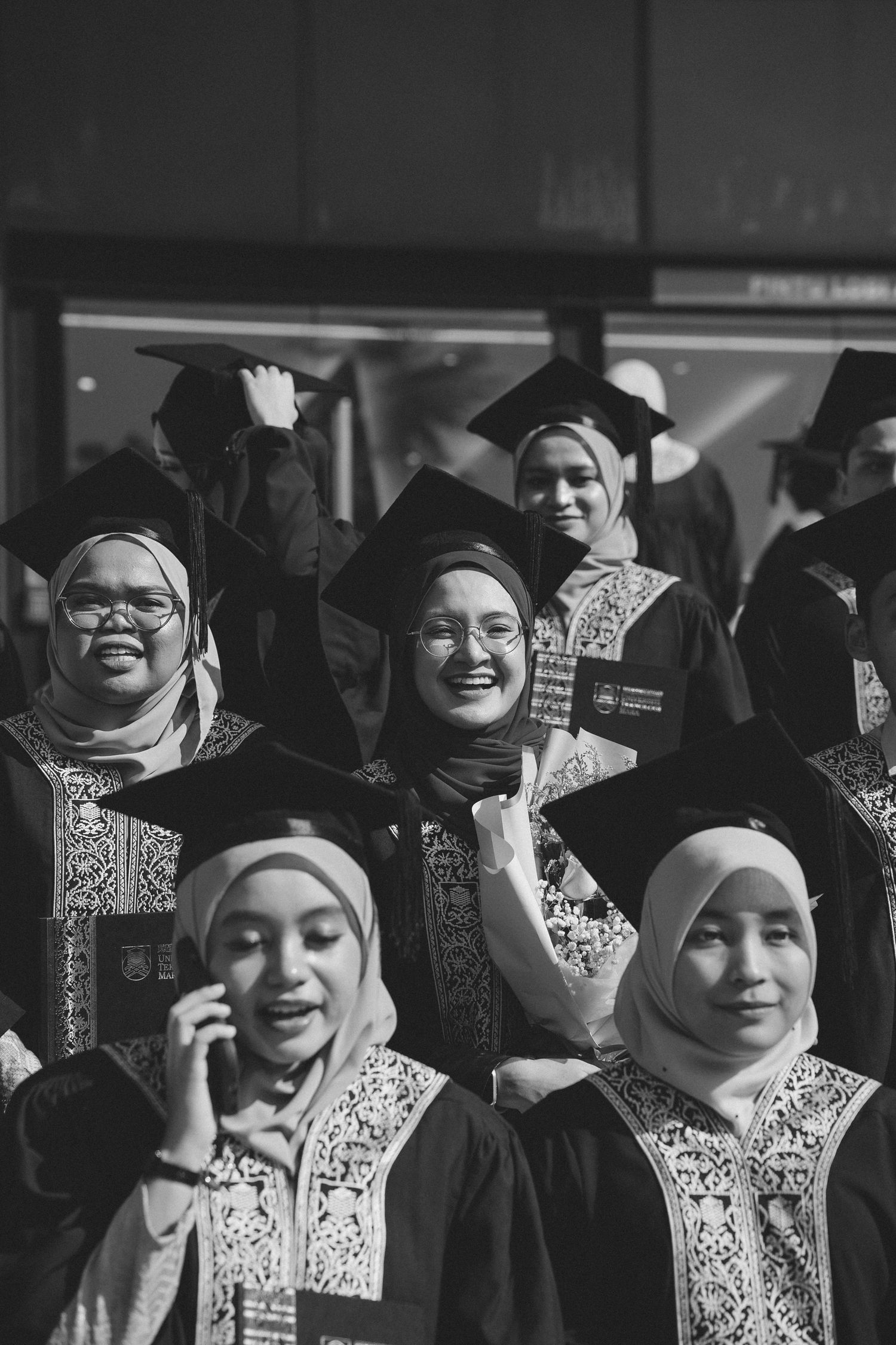 A group of graduates in traditional academic dress and hijabs celebrating at a graduation ceremony.