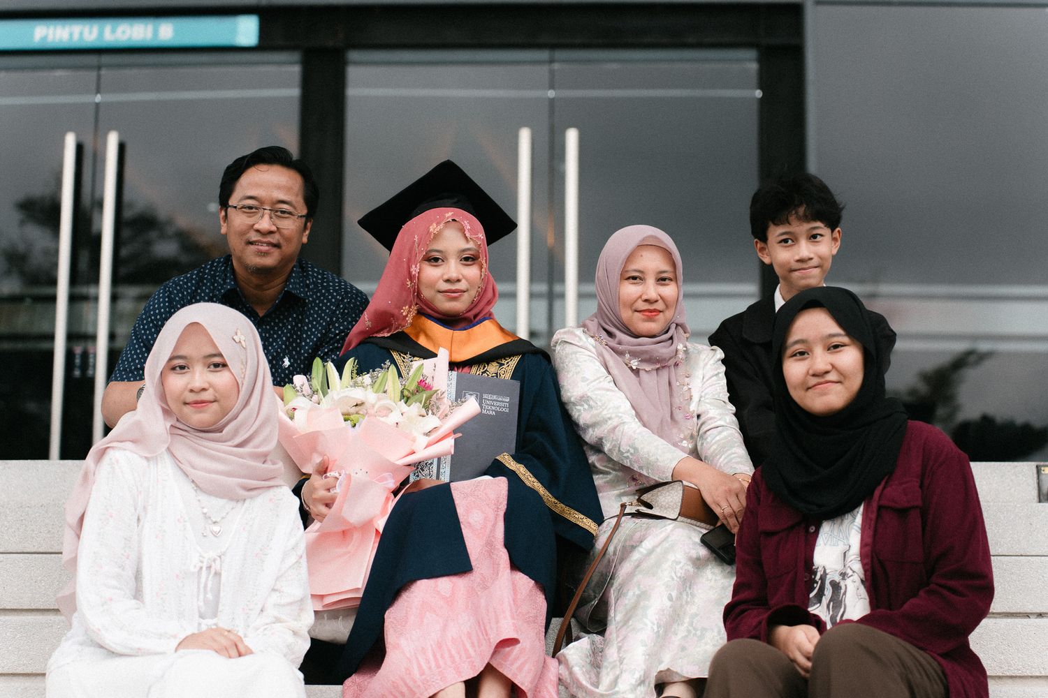 Family celebrating graduation with graduate in cap and gown holding flowers, posing together outdoors.