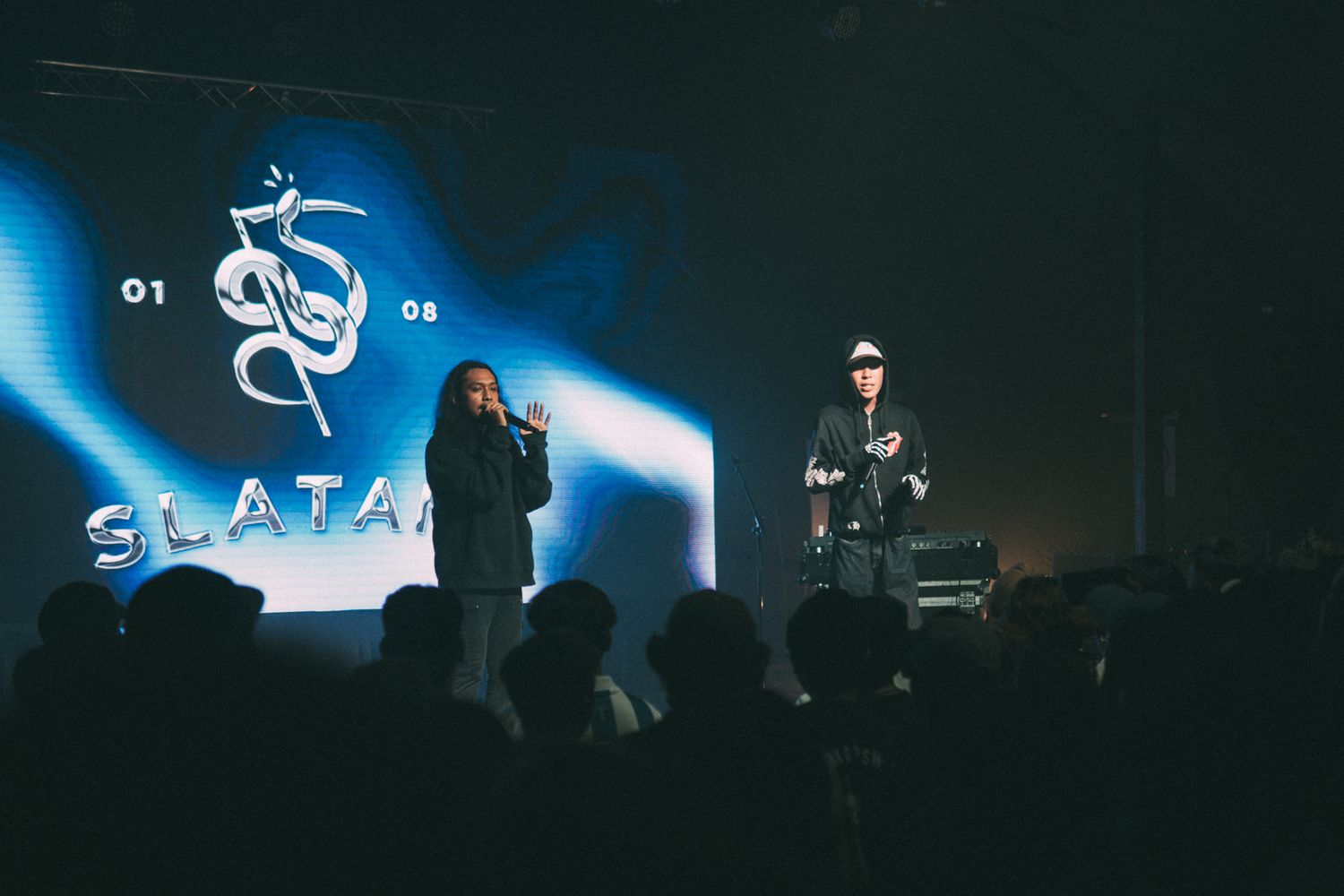 Concert stage with blue LED display and performers in low lighting.