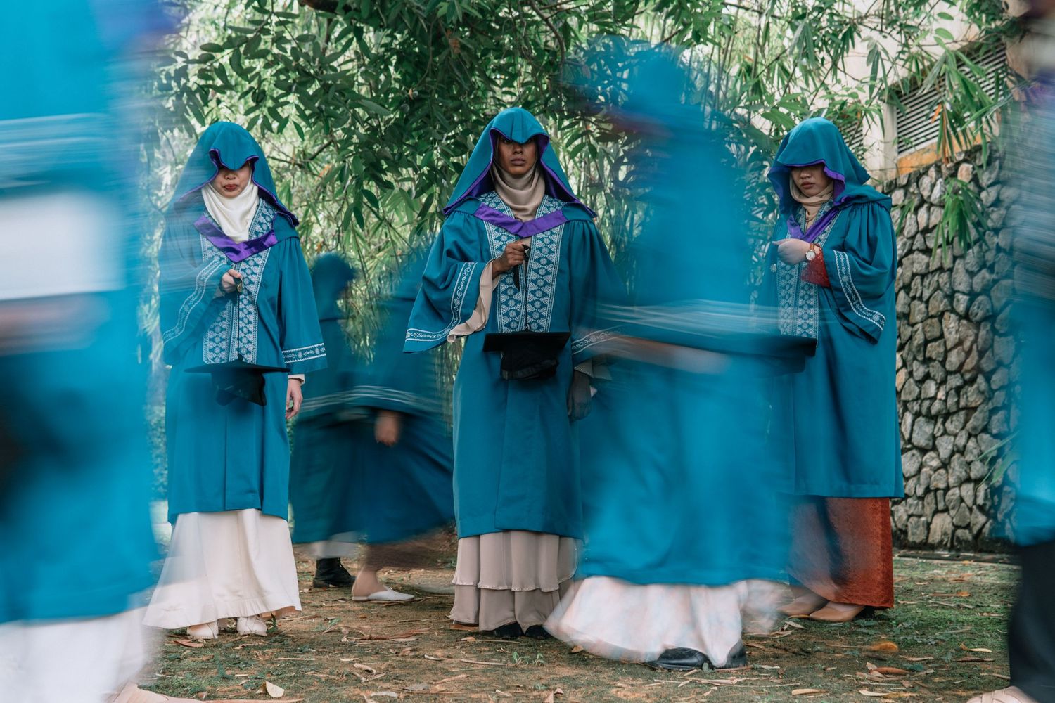 Three women in blue uniforms and hats standing against a bright blue wall.