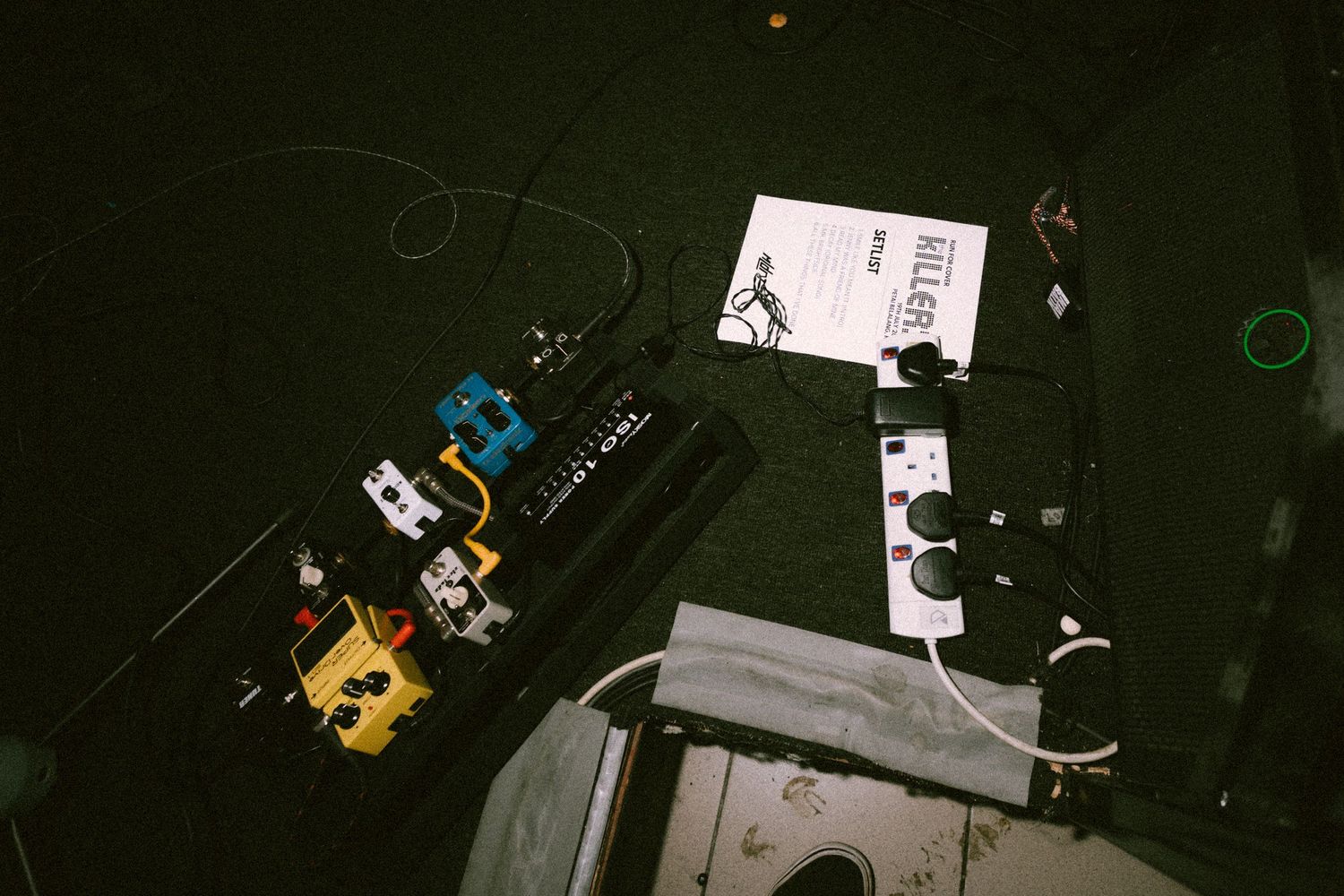 Guitar pedals and audio equipment scattered on a dark floor, captured from above with an analog film camera look.