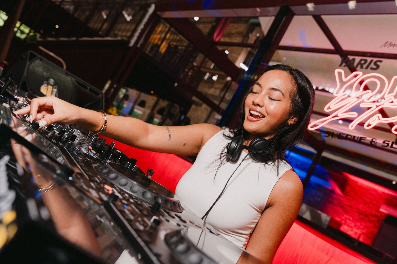 DJ performs at a nightclub with vibrant red lighting and professional equipment setup.