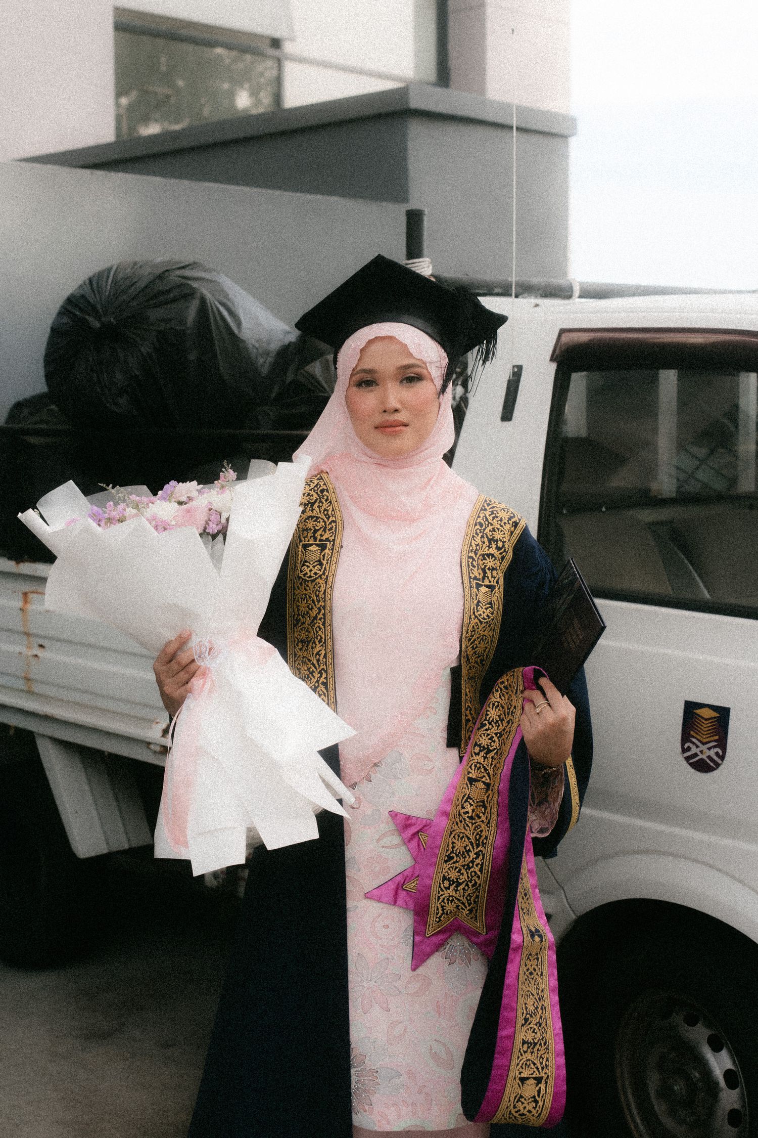 People in traditional Middle Eastern dress holding papers while standing near parked vehicles.