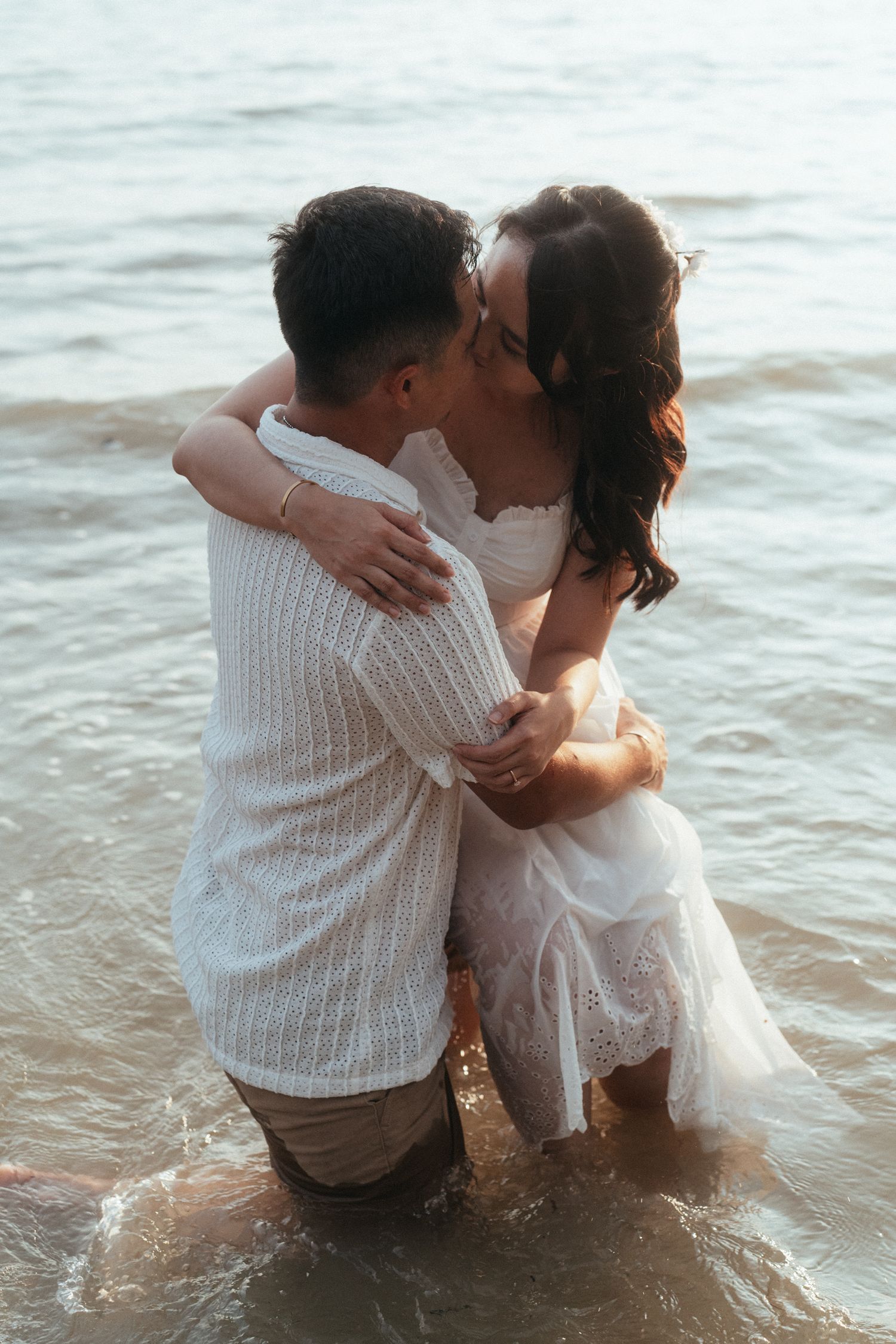 A romantic couple embracing in the ocean waves during sunset.