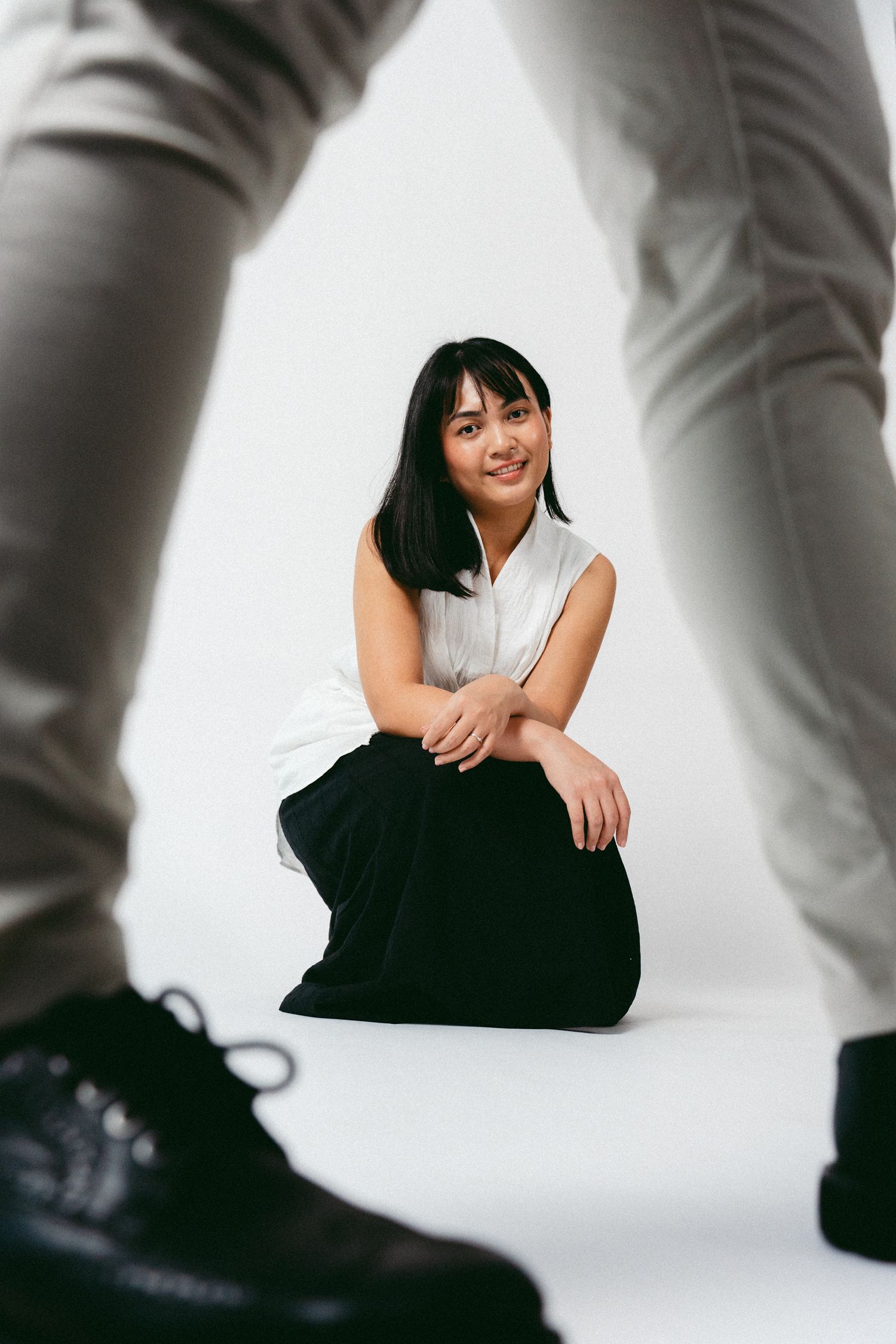 An artistic low angle shot of someone sitting on white background framed by legs and shoes.