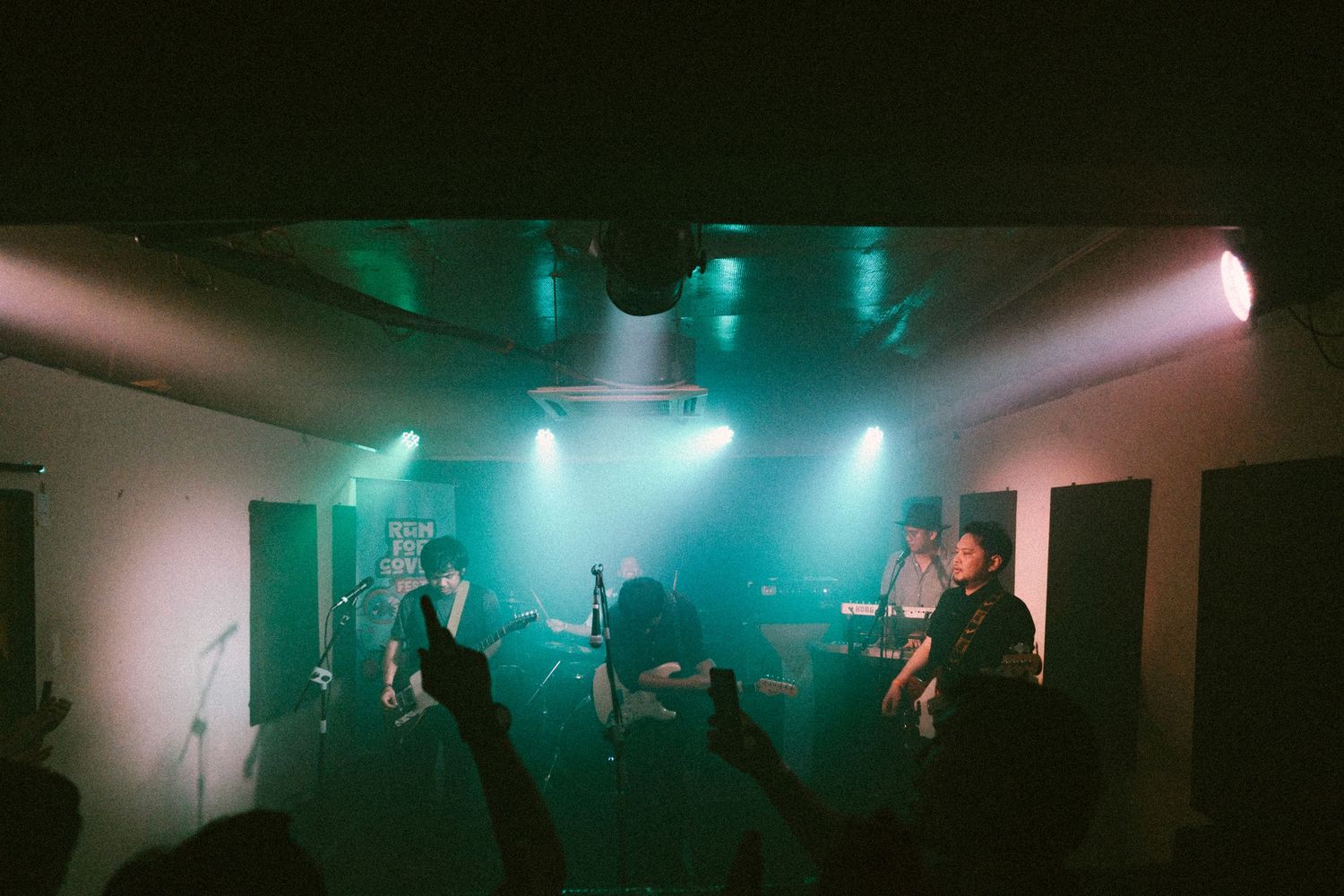 Band performing on stage with atmospheric turquoise lighting and fog creating moody concert ambiance.
