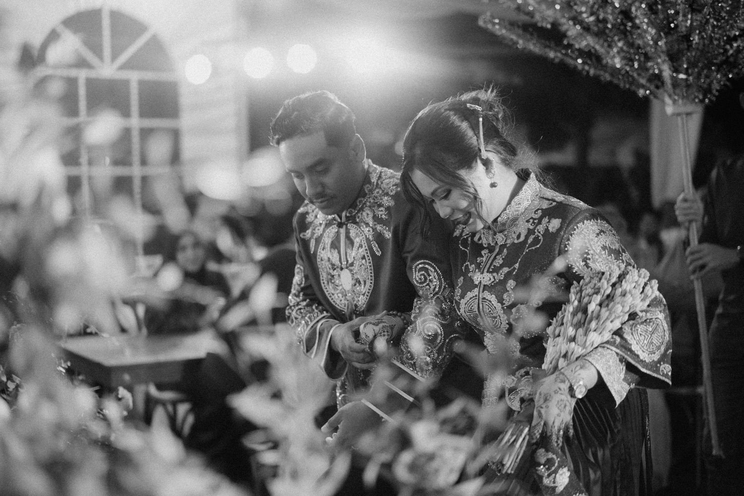 Two people in patterned outfits play acoustic guitars together in a black and white artistic photograph.
