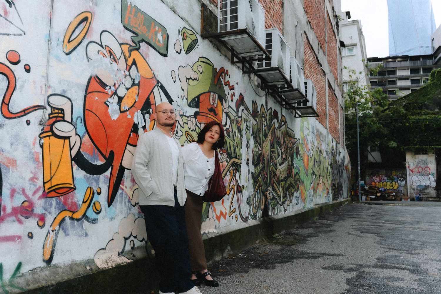 Two people posing in front of a vibrant colorful graffiti mural wall in an urban alleyway.