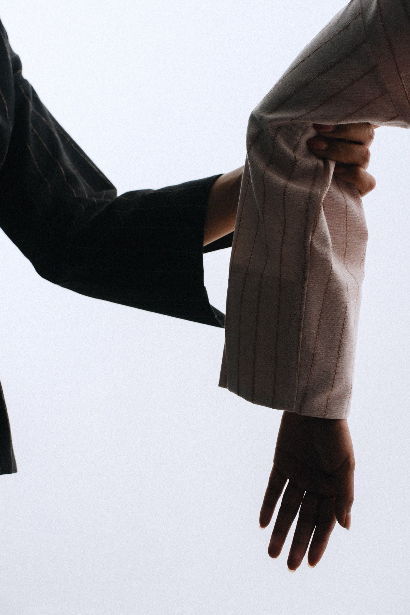 Two people gripping each other's suit sleeves in a dramatic low-angle shot against a pale sky.