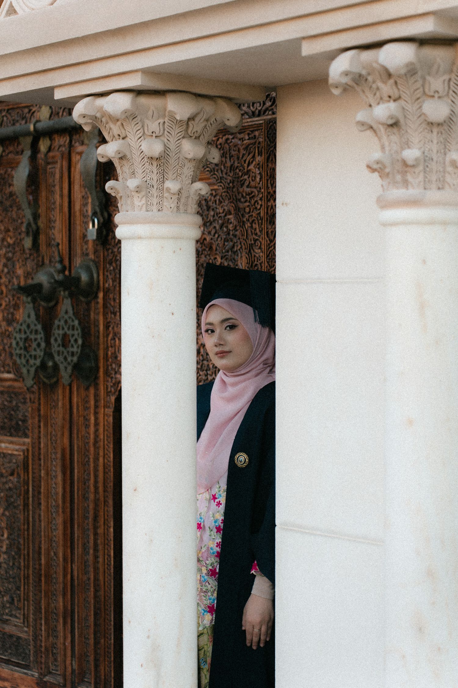 A woman in a pink hijab and black outfit poses between white architectural columns in a sequence of similar shots.