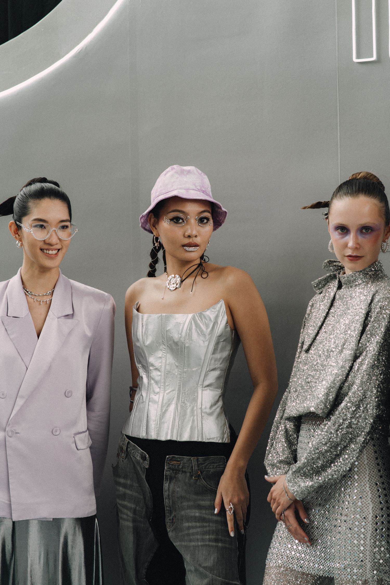 Three models pose in modern fashion looks including blazer, corset and sparkly dress.