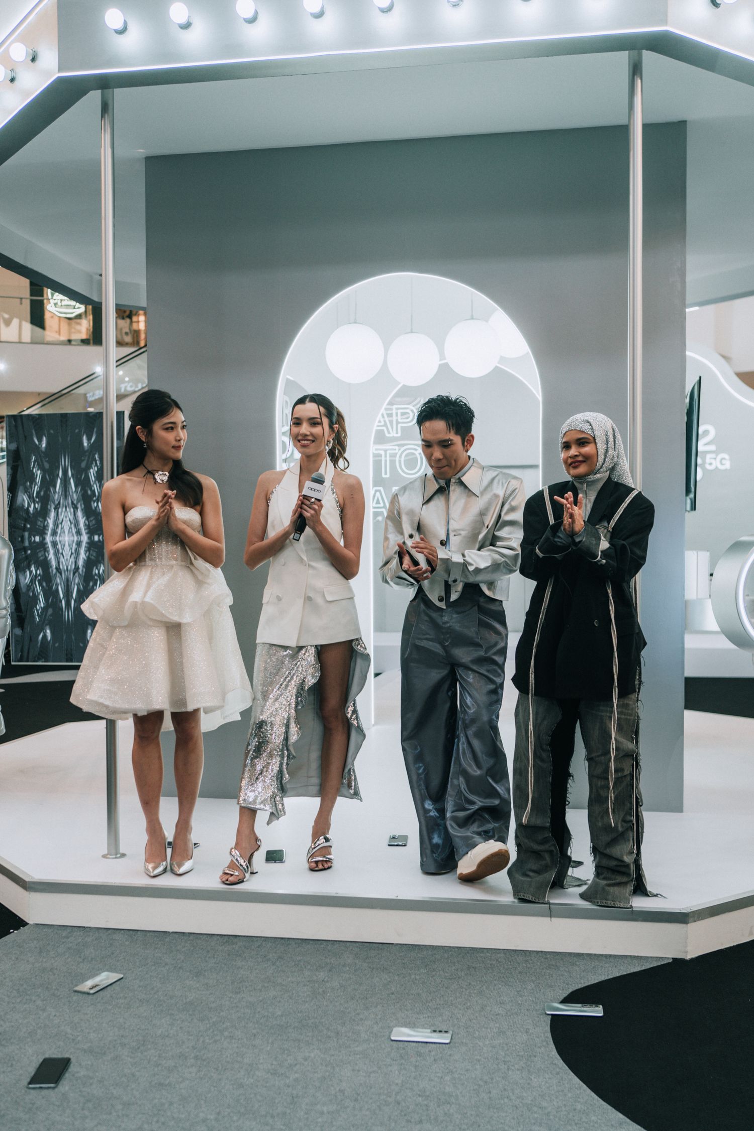 Models posing together on a raised platform under a modern white archway with illuminated globes.