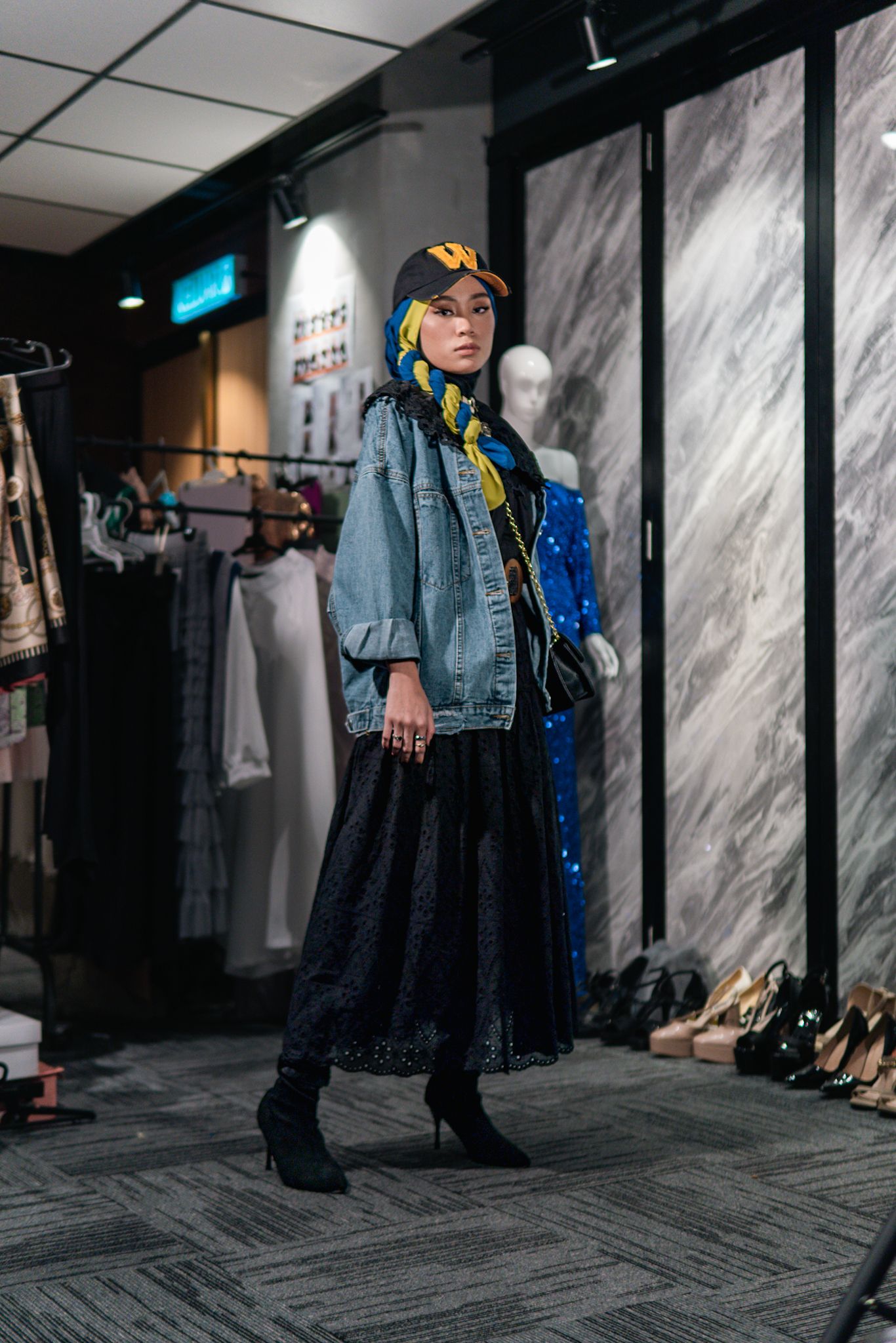 Street style outfit featuring denim jacket and black lace skirt with boots on gray carpeted floor.