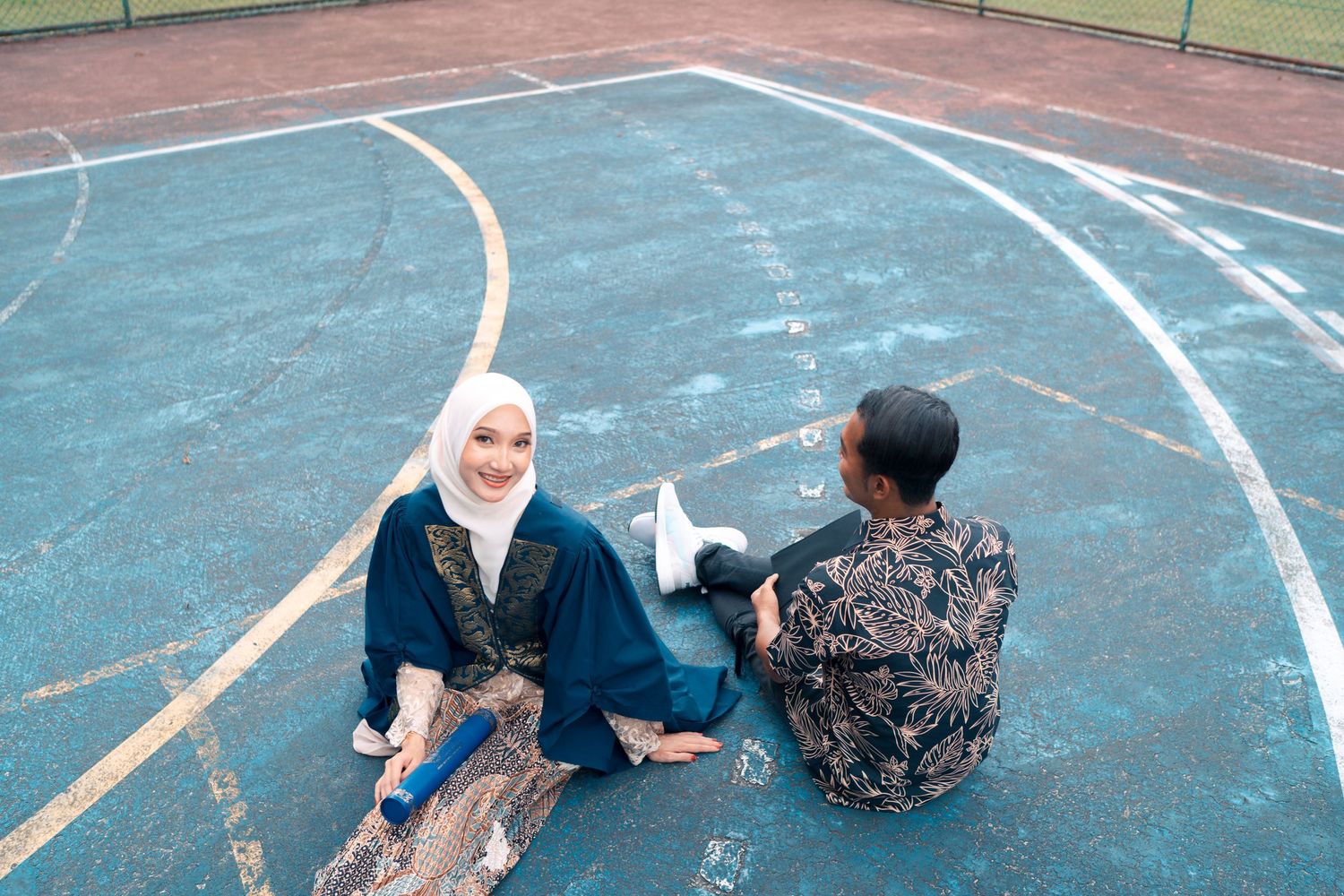 Two graduates sit and chat on outdoor running track.