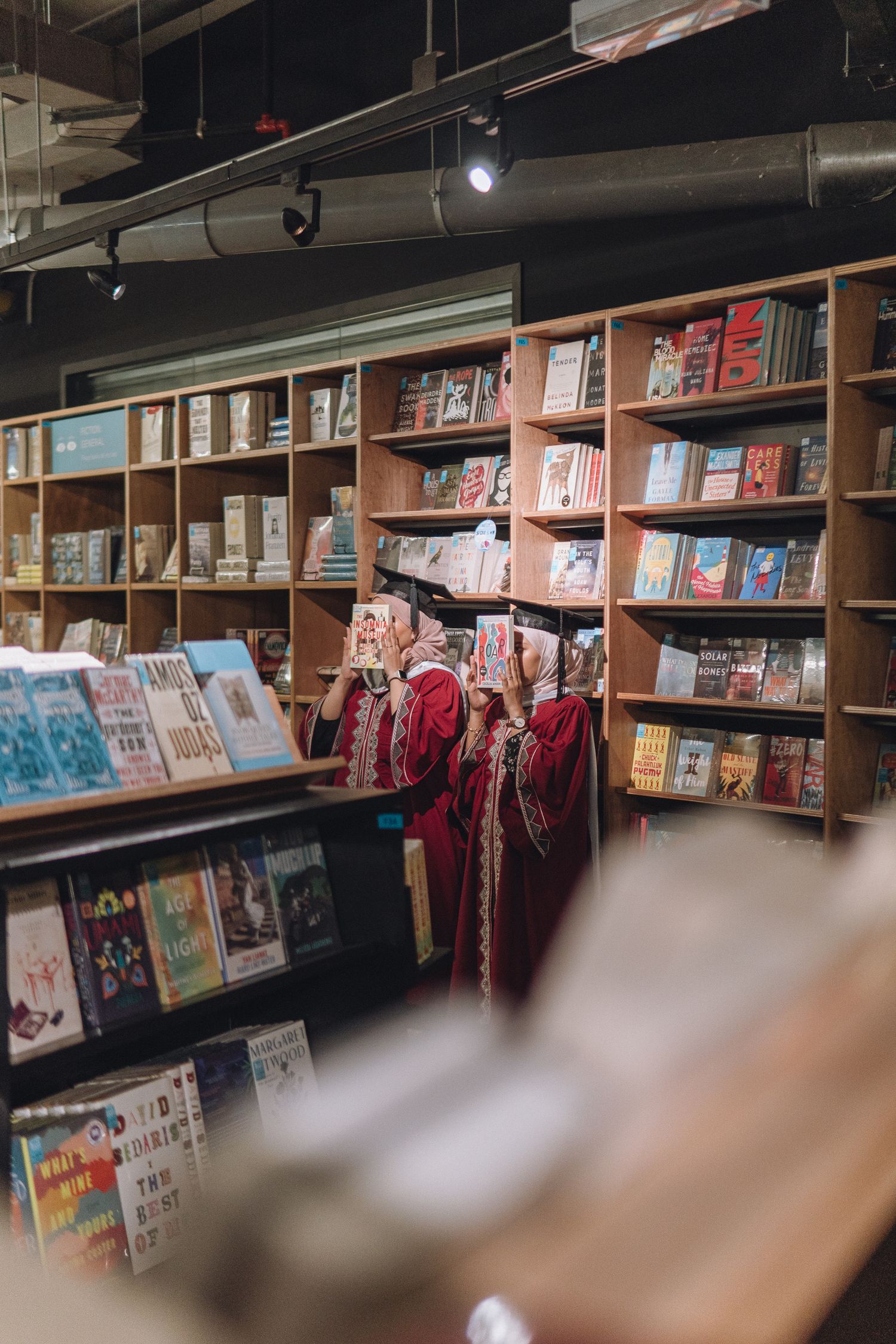 A shelf of books in a bookstore with figures in red graduation robes browsing the selection.