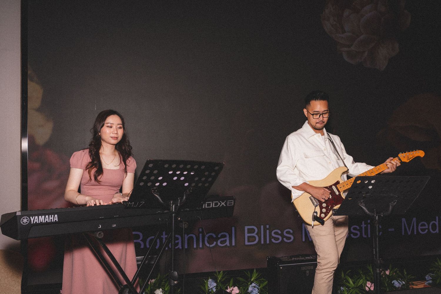 Musicians perform on stage with a woman playing keyboard and a man playing electric guitar during a live performance.