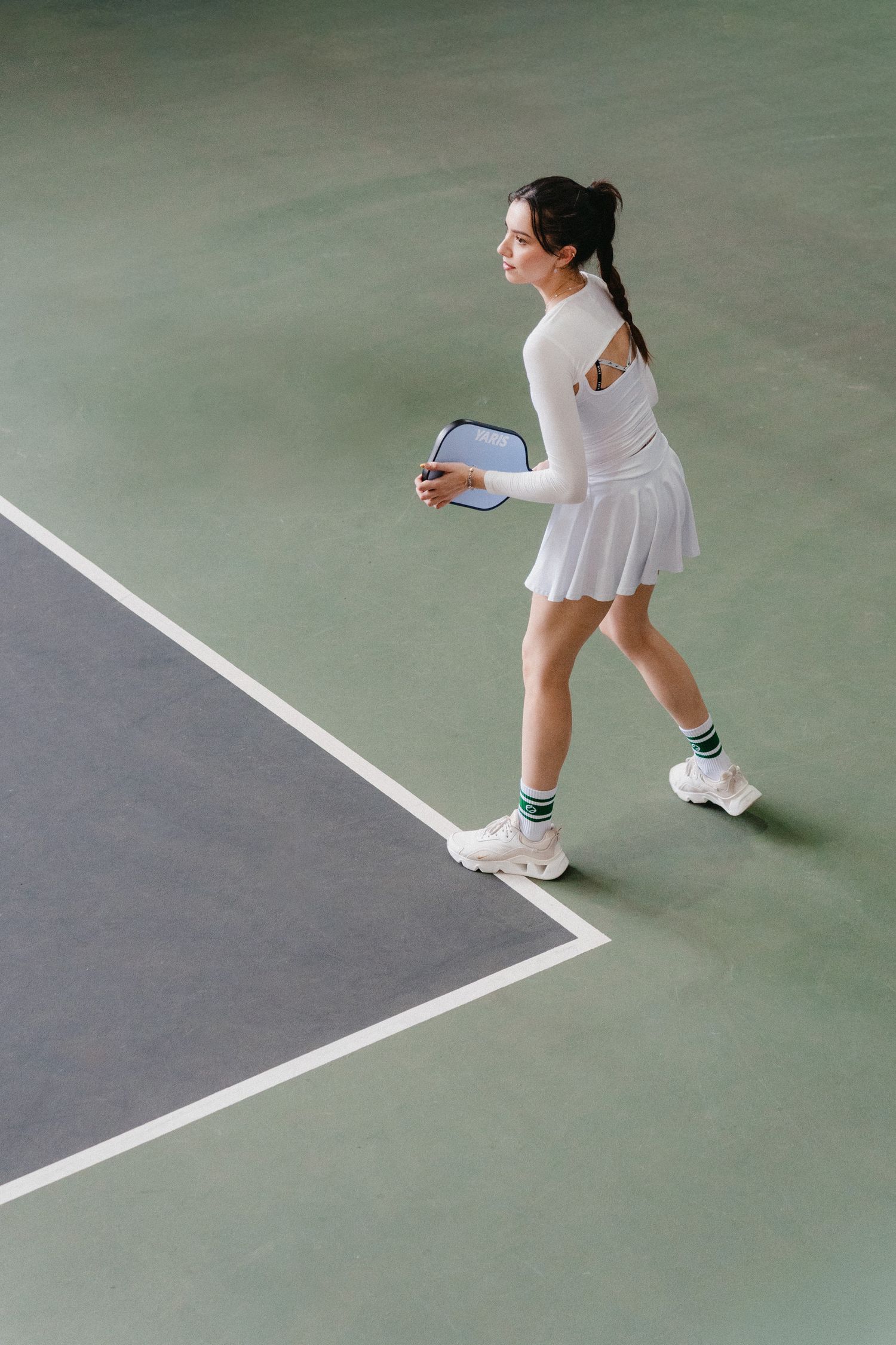 Close-up view of tennis player's feet in white shoes and dress following court lines during a match.