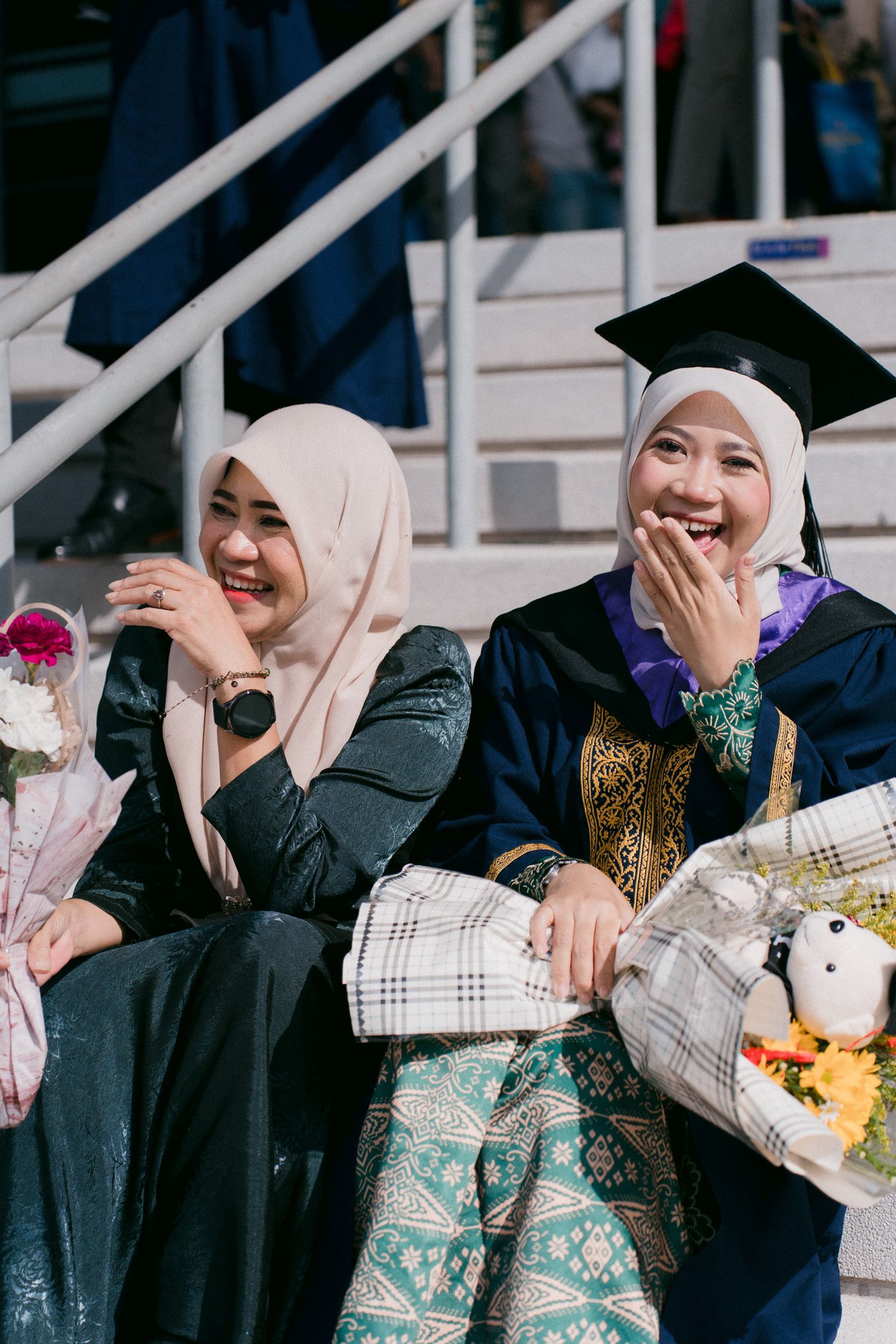 A group of women wearing white hijabs and traditional dress sit together while covering their faces with their hands.