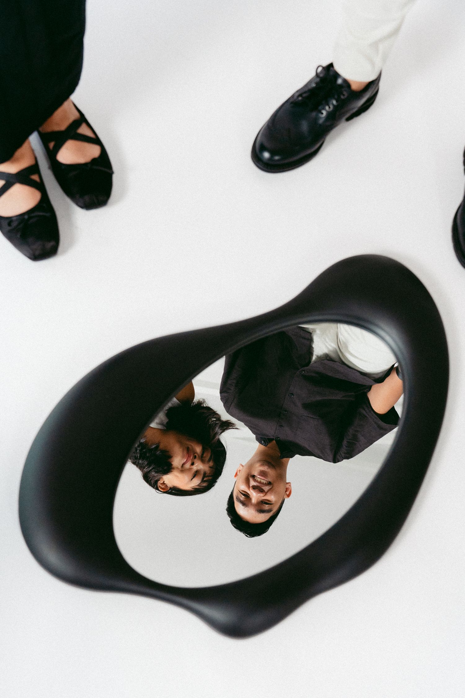 An artistic overhead view of a couple reflected in a curved black mirror on white background.