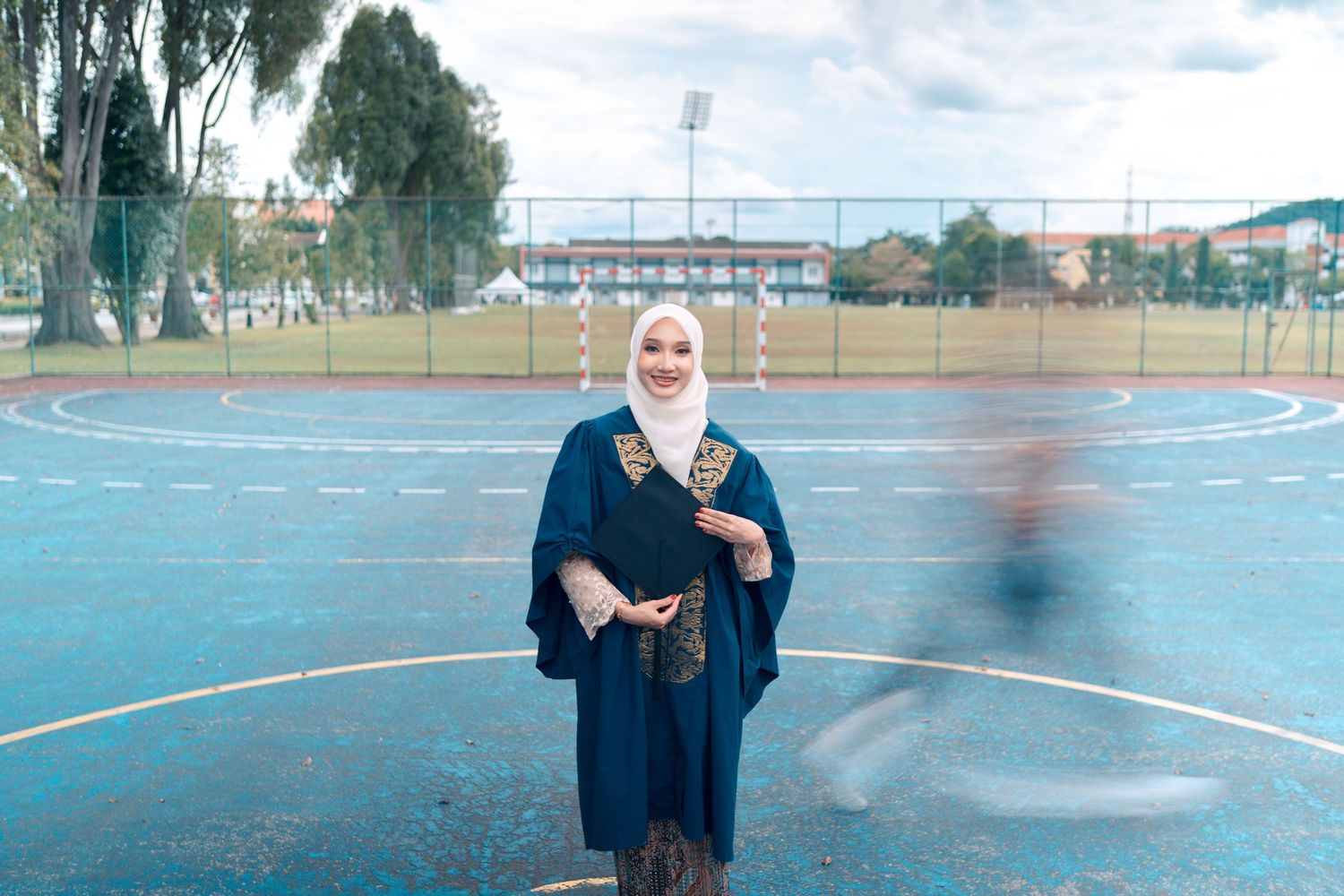 Graduate standing on outdoor basketball court wearing traditional academic regalia.