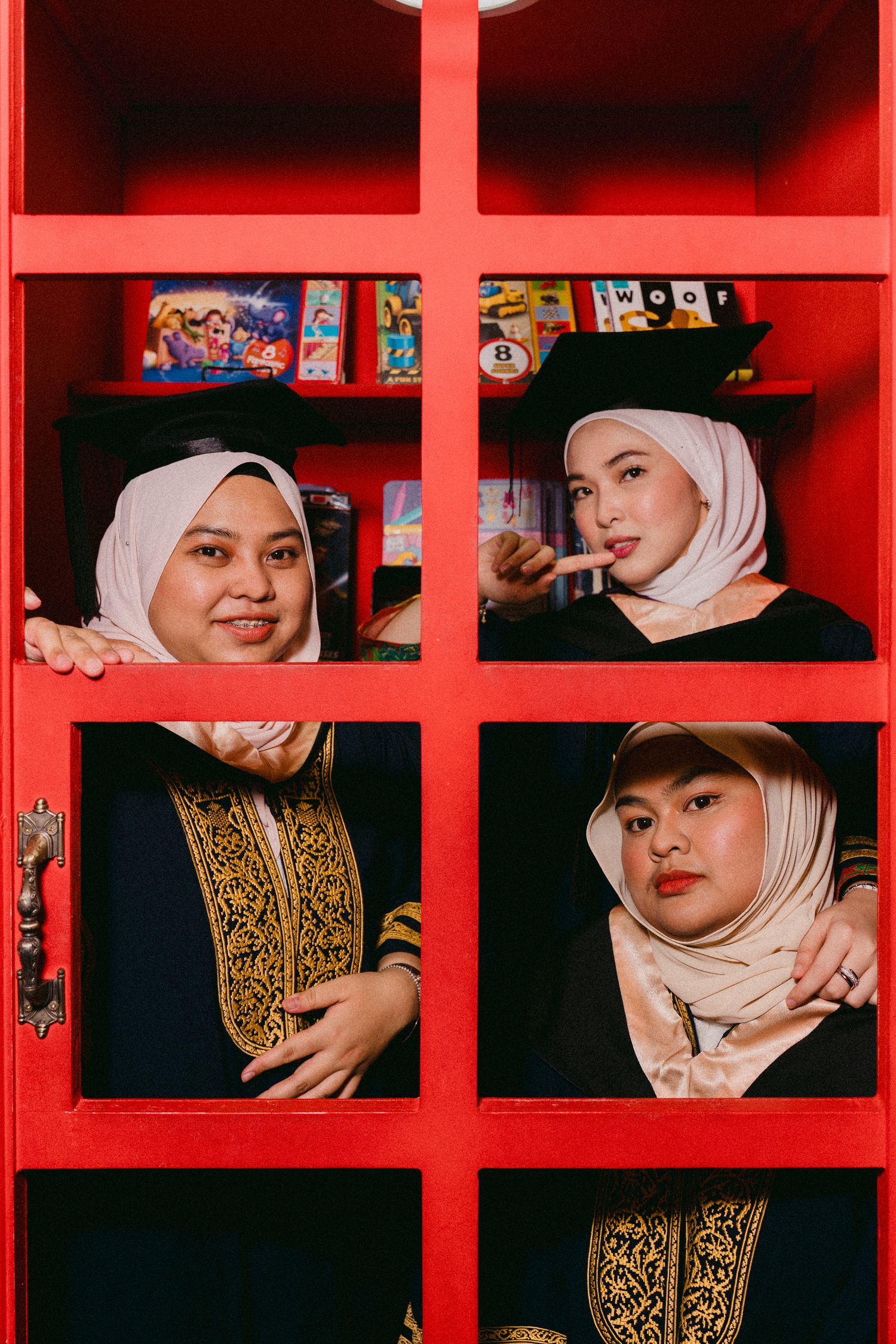 Creative graduation photo showing graduates posing in red window-like frame with books.