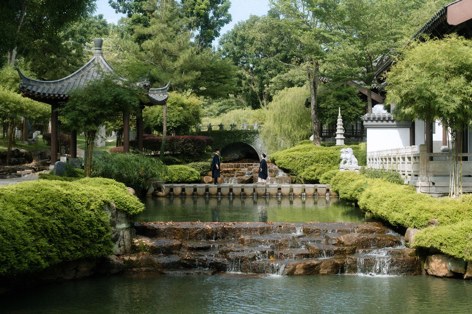 Serene Chinese garden with pagoda, stone waterfall, lush greenery, and tranquil pond reflecting traditional Asian architecture.
