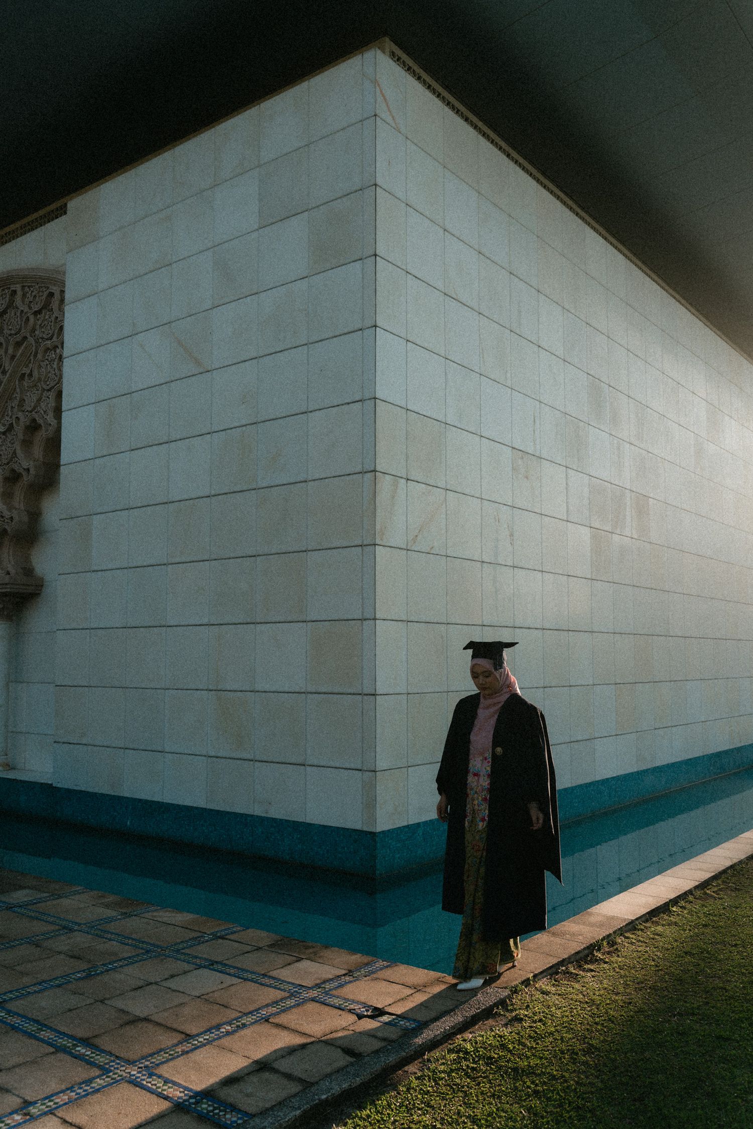 A graduate in academic regalia walks along a white wall casting dramatic shadows in a sequence of architectural photos.