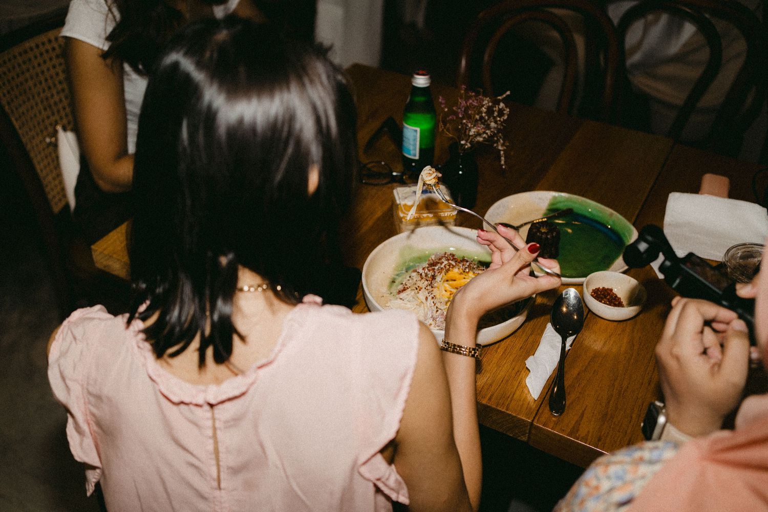 People gather around a wooden table with food and drinks for a casual dining experience.