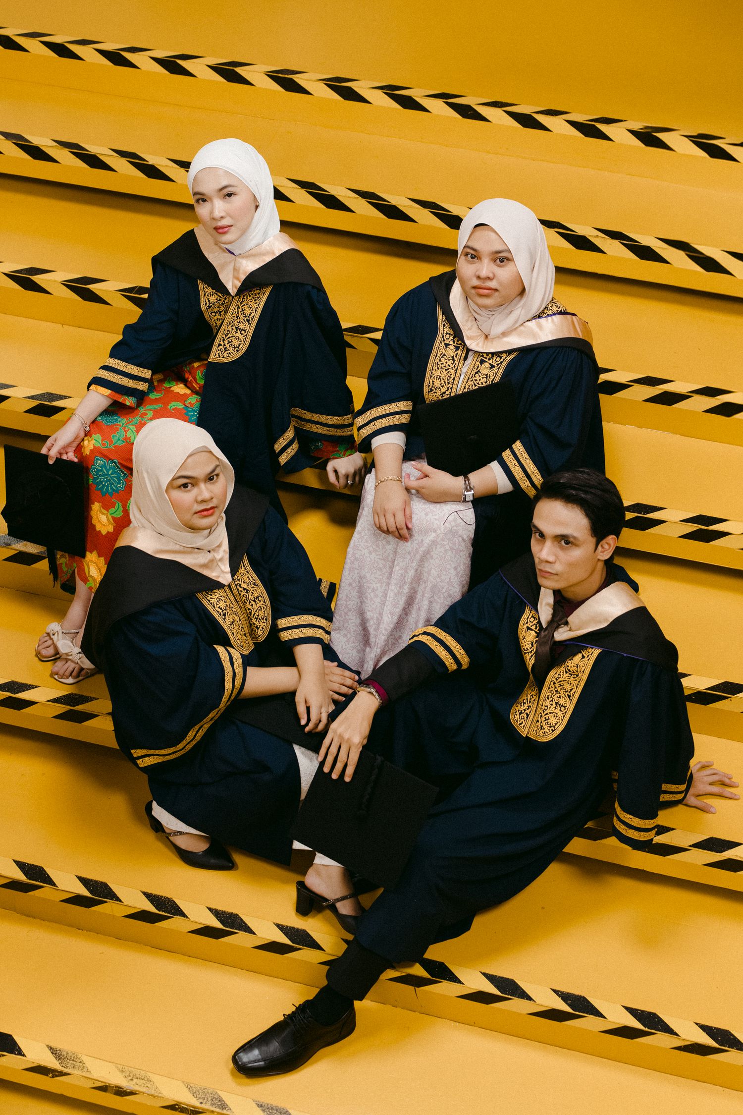 Group photo of graduates in matching black and gold robes against yellow background with striped pattern.