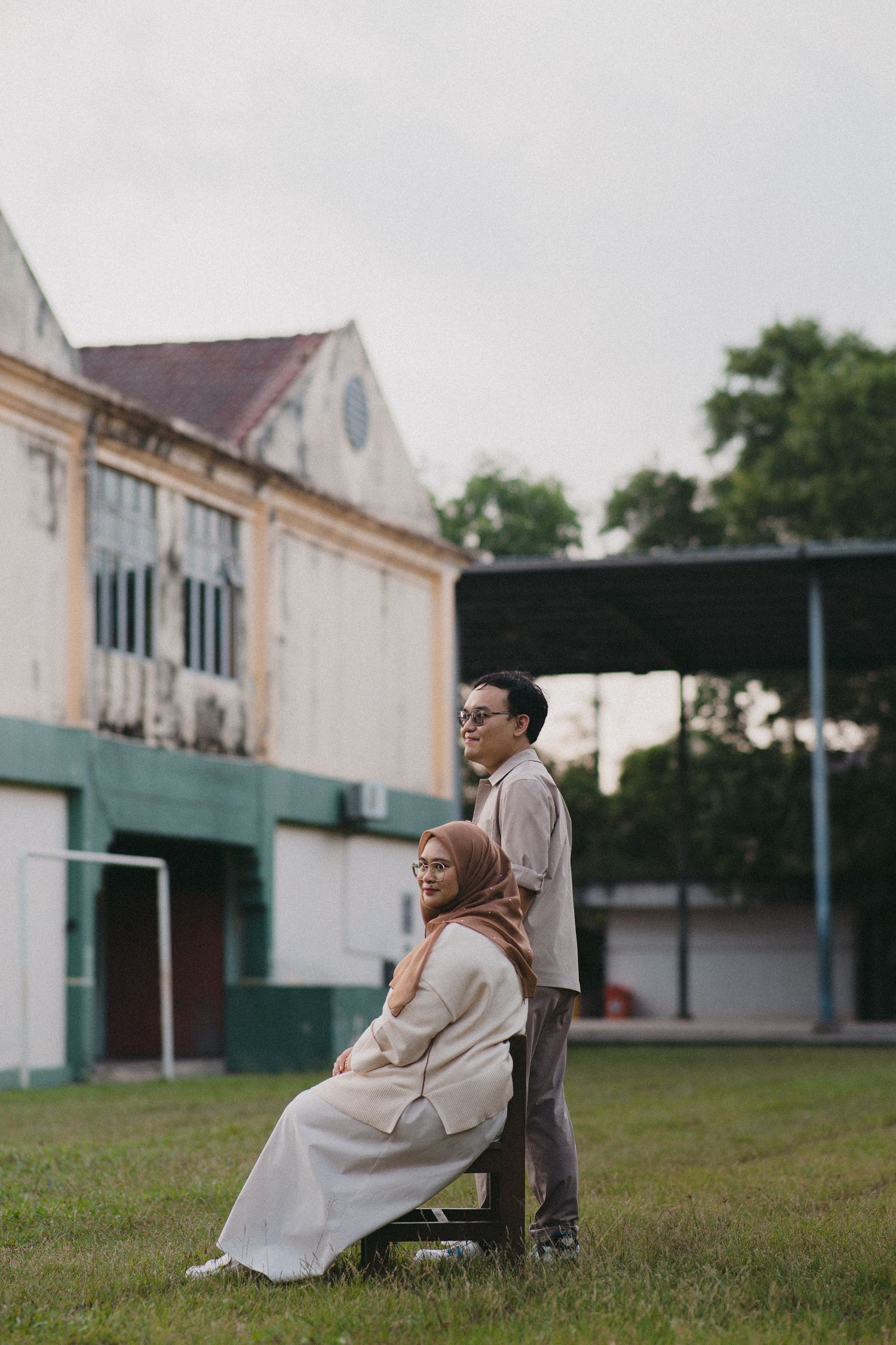 Couple in casual attire posing together outdoors with vintage building in background.