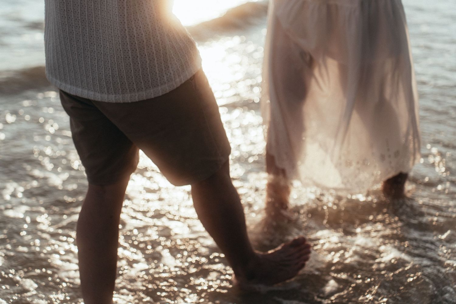 Two people standing in shallow ocean water during golden hour.