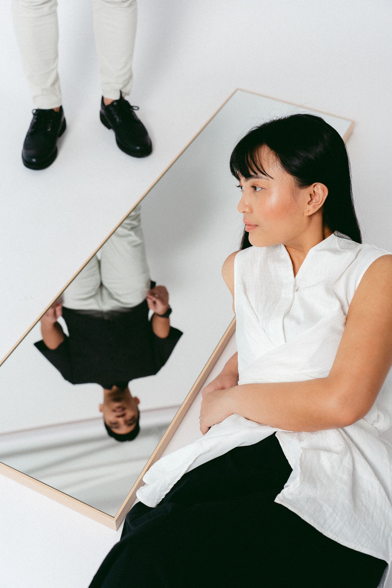 A creative portrait with a person in white sitting next to an angled mirror reflection.
