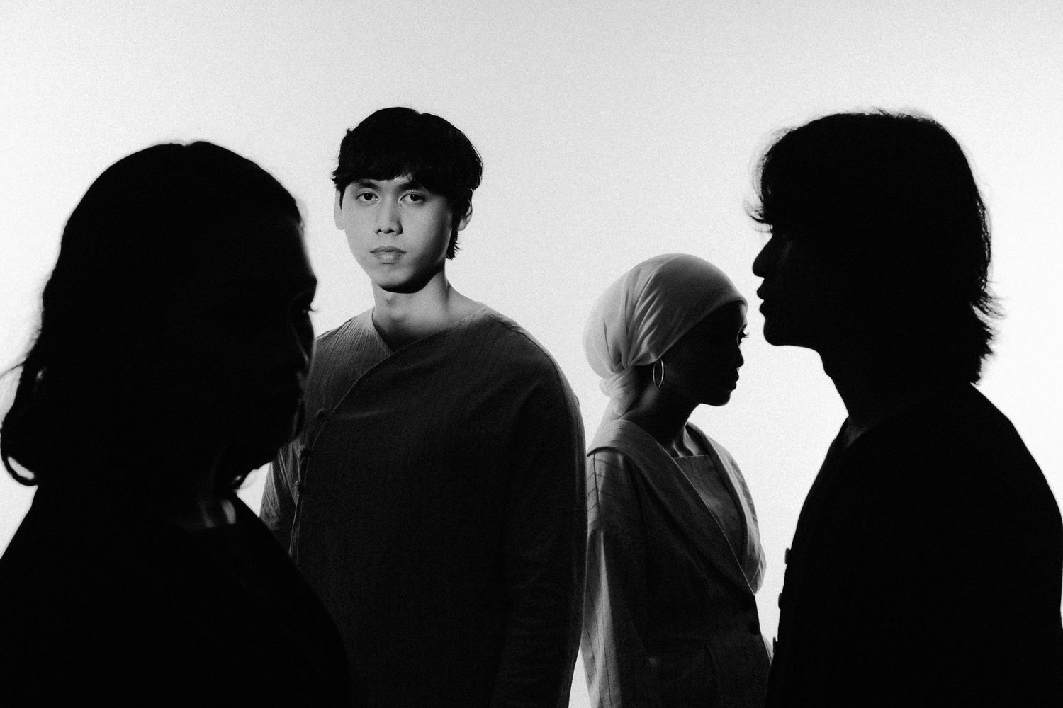 Black and white photo of four people, one illuminated young man centered among three shadowy silhouettes.