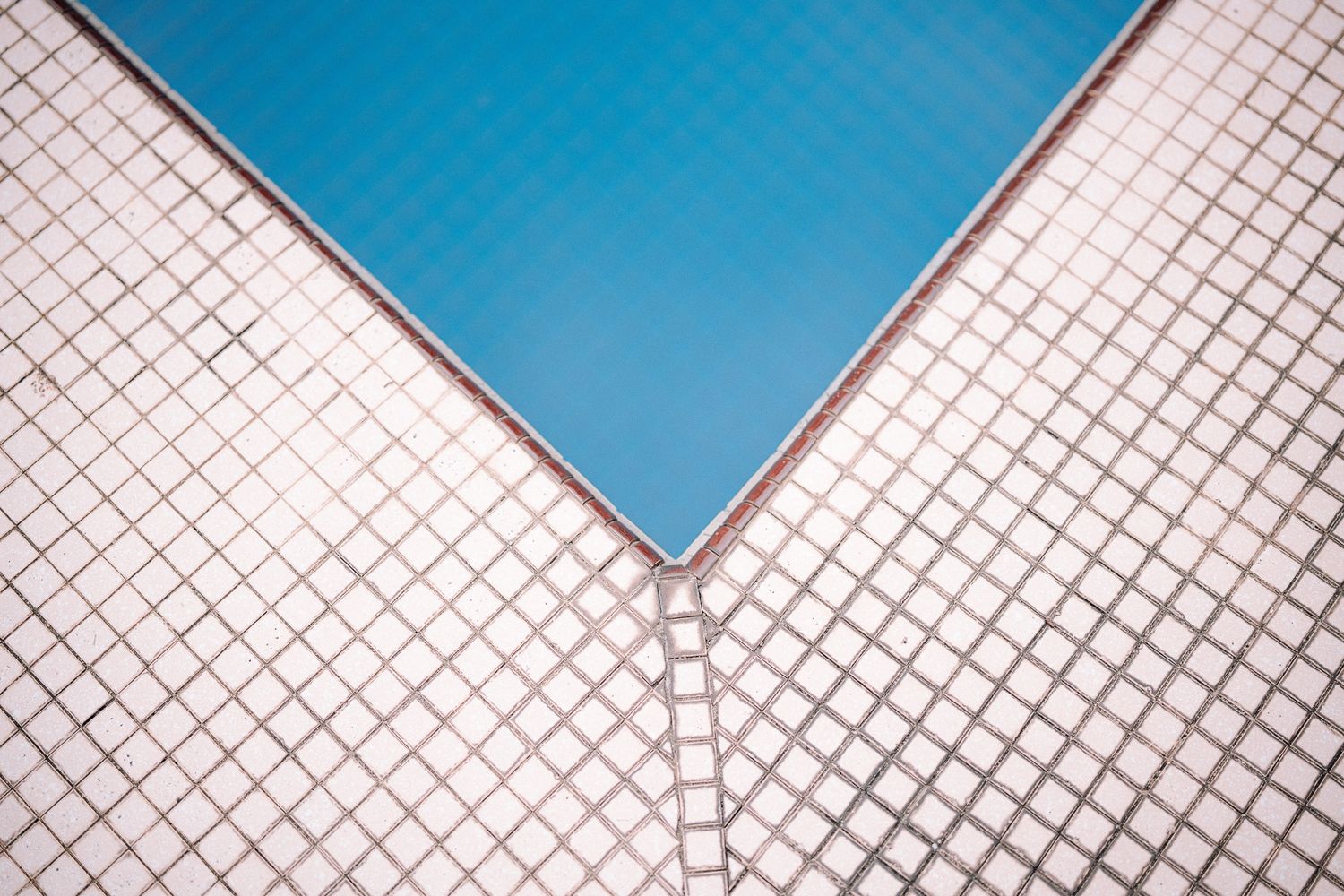 Blue swimming pool corner with white mosaic tile surround, geometric minimalist design.