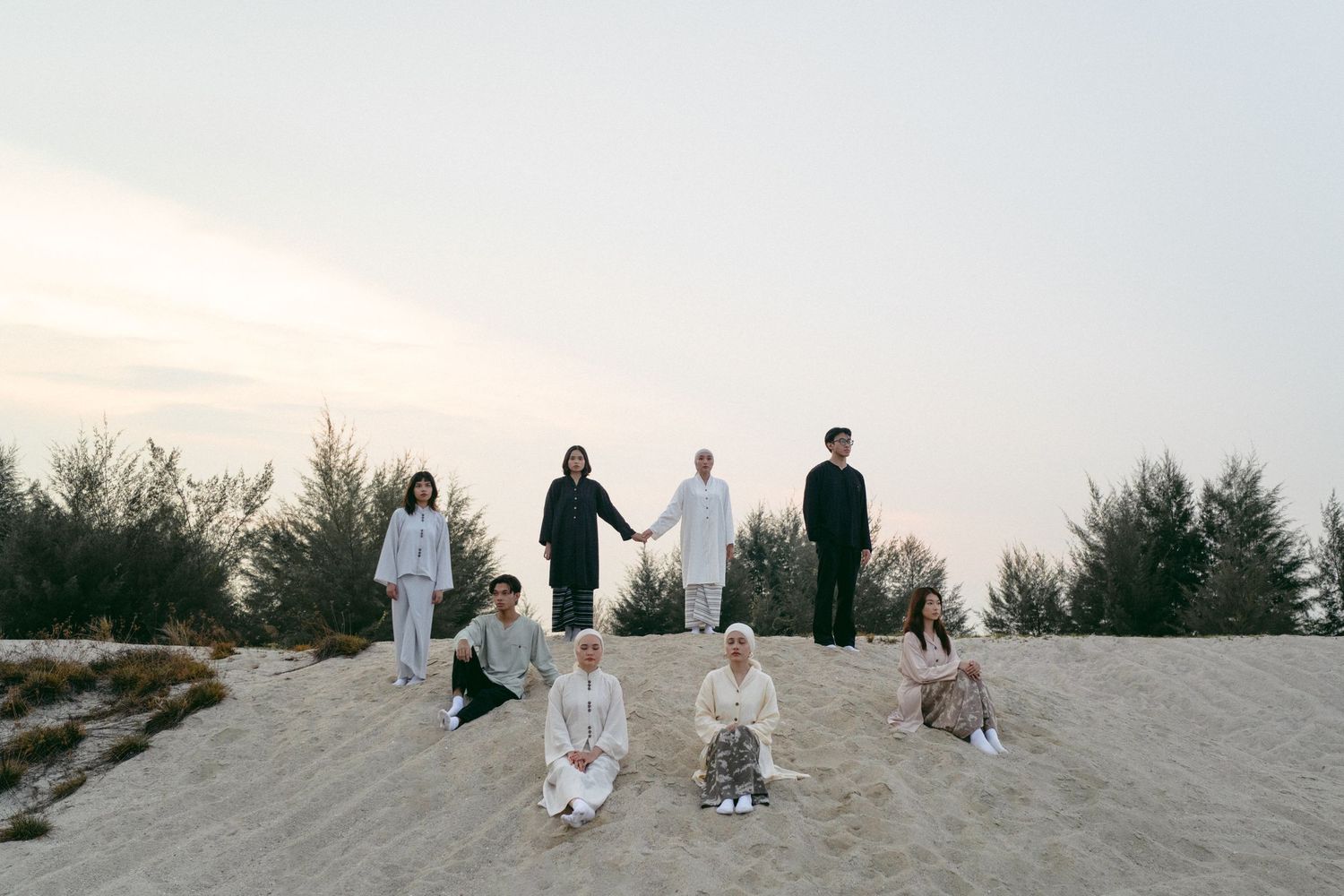 Group photo of people and dogs standing together on a sandy hill at sunset.