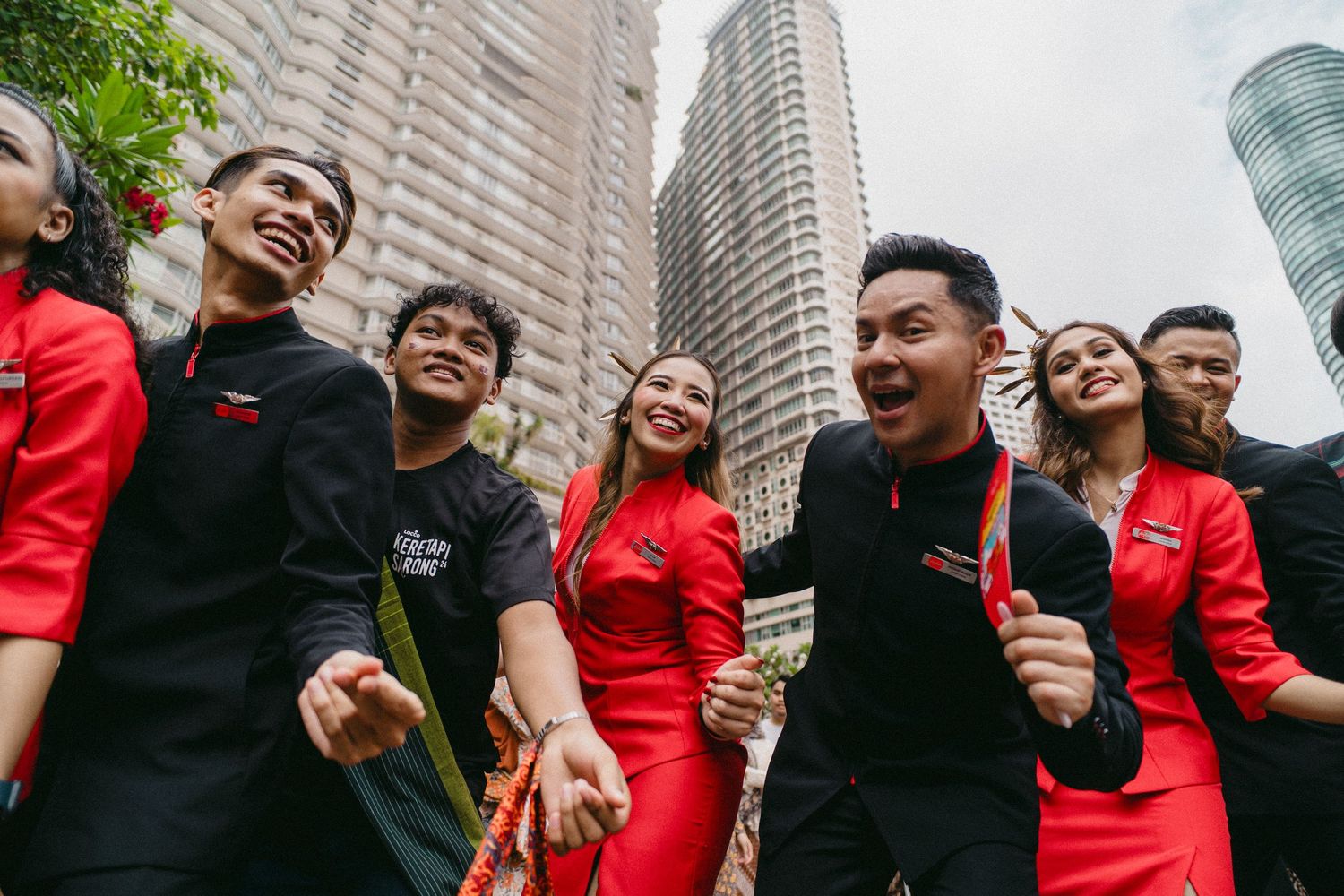Group in red and black uniforms smiling enthusiastically against urban skyline backdrop.