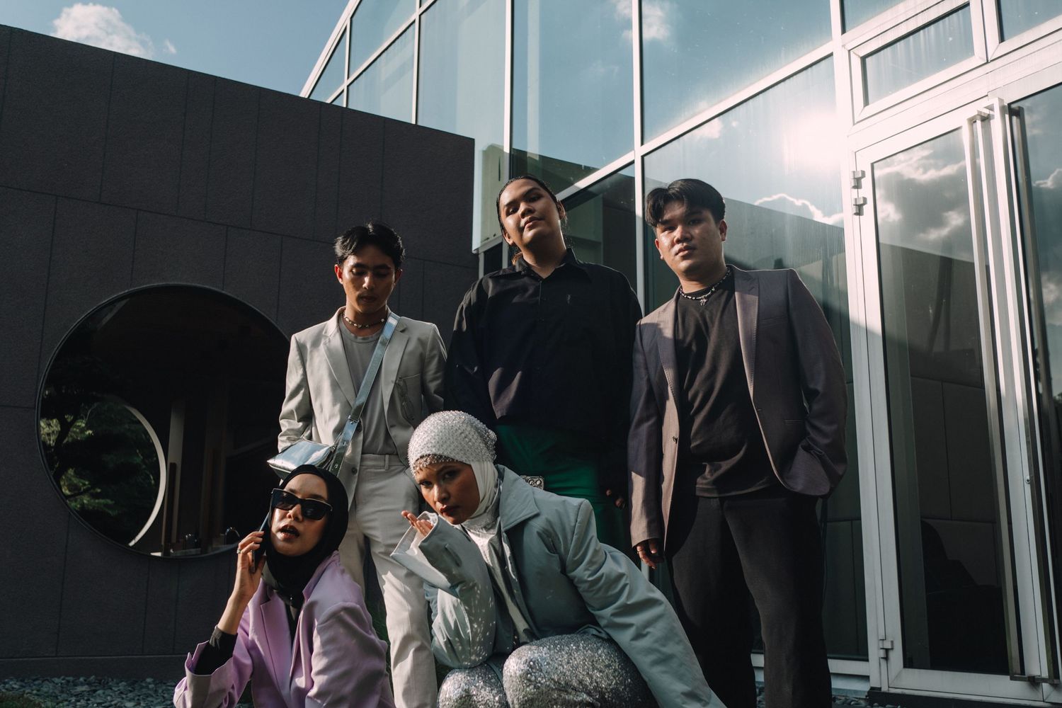 Group photo of fashion models posing outside modern glass building.