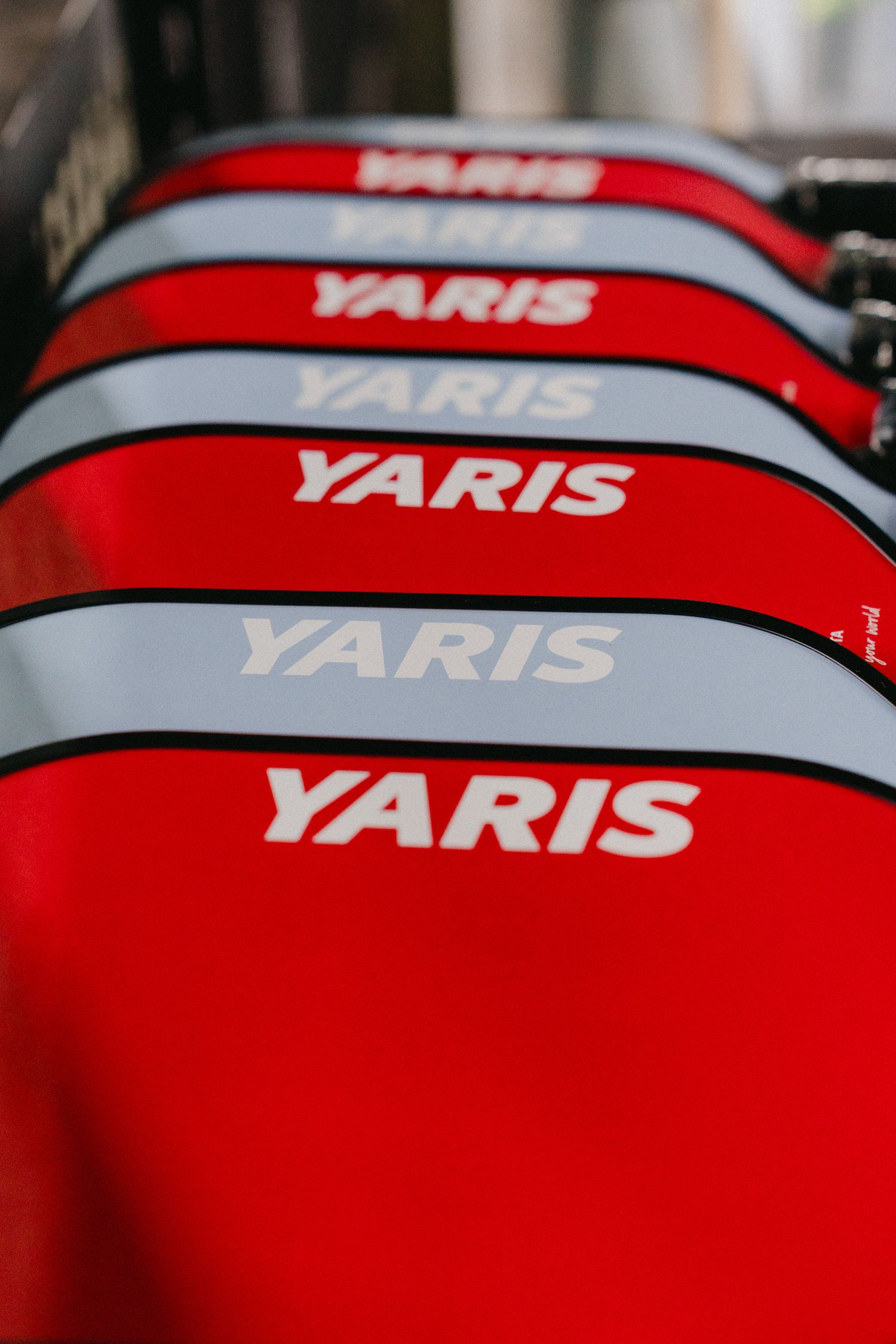 A row of bright red Toyota Yaris vehicles with white lettering parked in sequence showing repeating brand text.