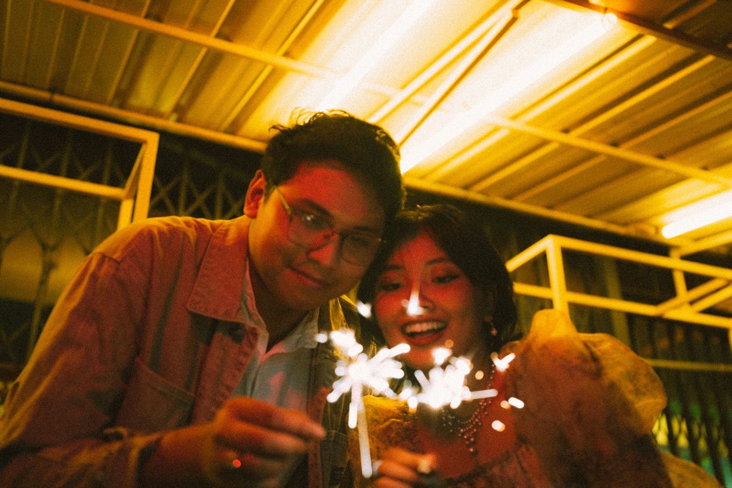 Couple holding sparklers at night with warm lighting creating a festive atmosphere.