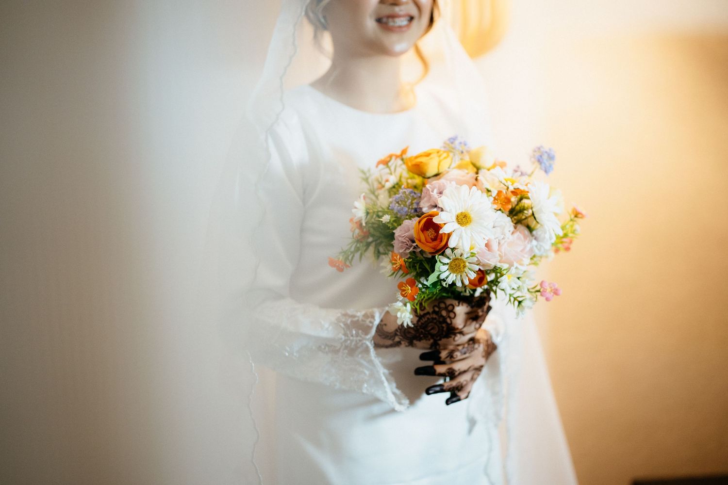 A bride in a flowing white wedding dress holds a beautiful bouquet of wildflowers against a warm glowing background.