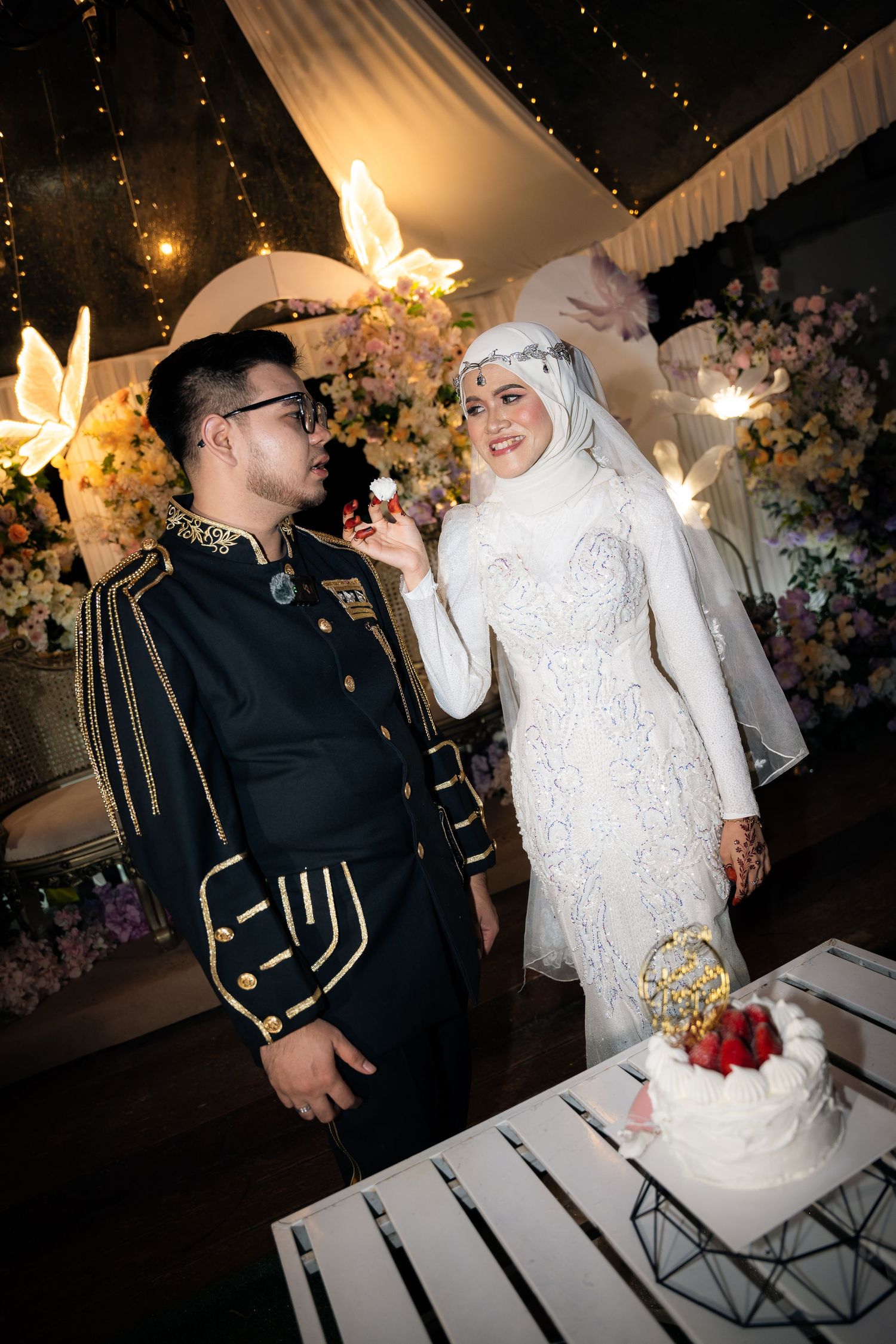 A joyful wedding celebration with a couple in traditional white and military dress attire sharing a moment by their cake.