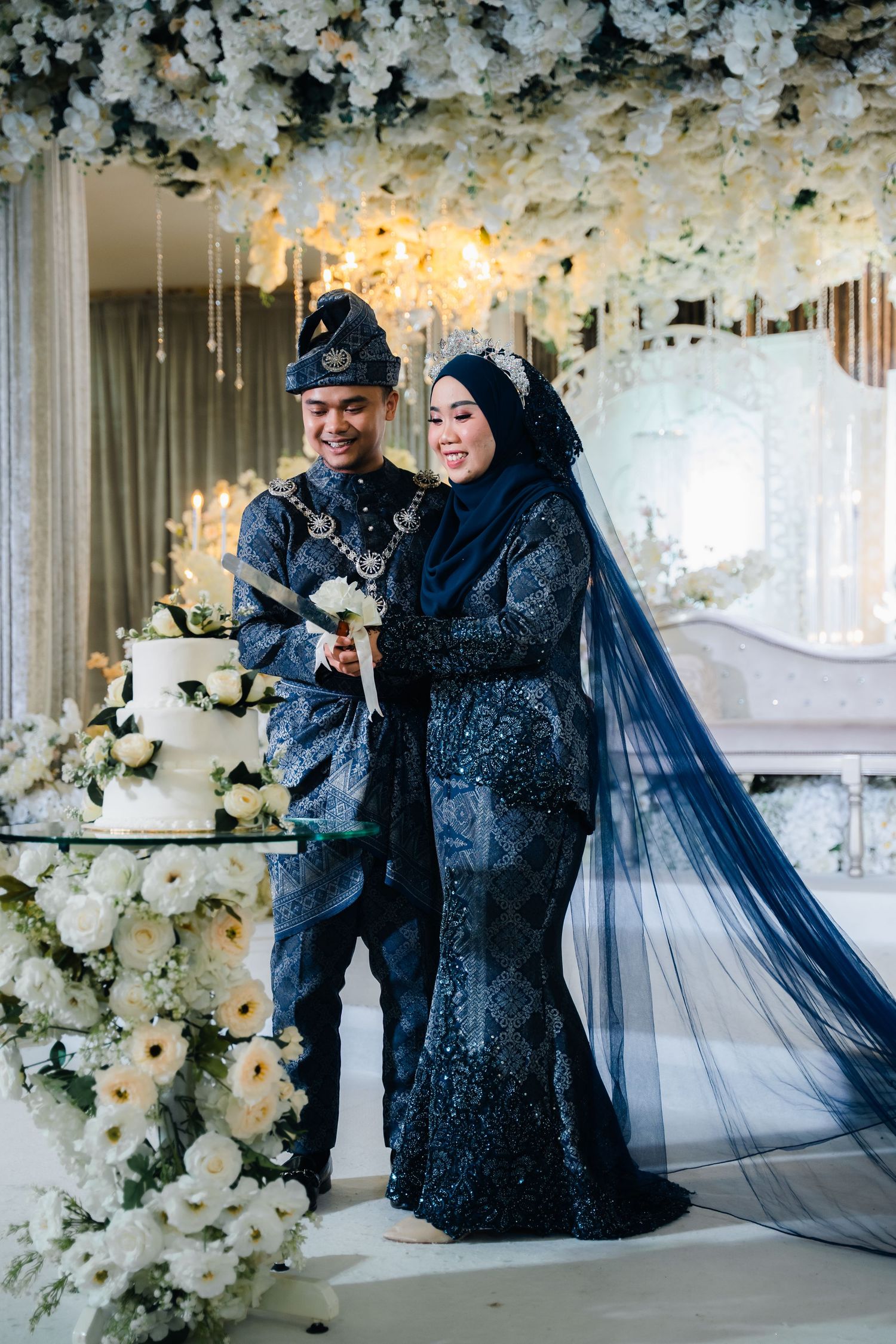 Navy blue lace formal dress and veil photographed in elegant white floral venue setting.