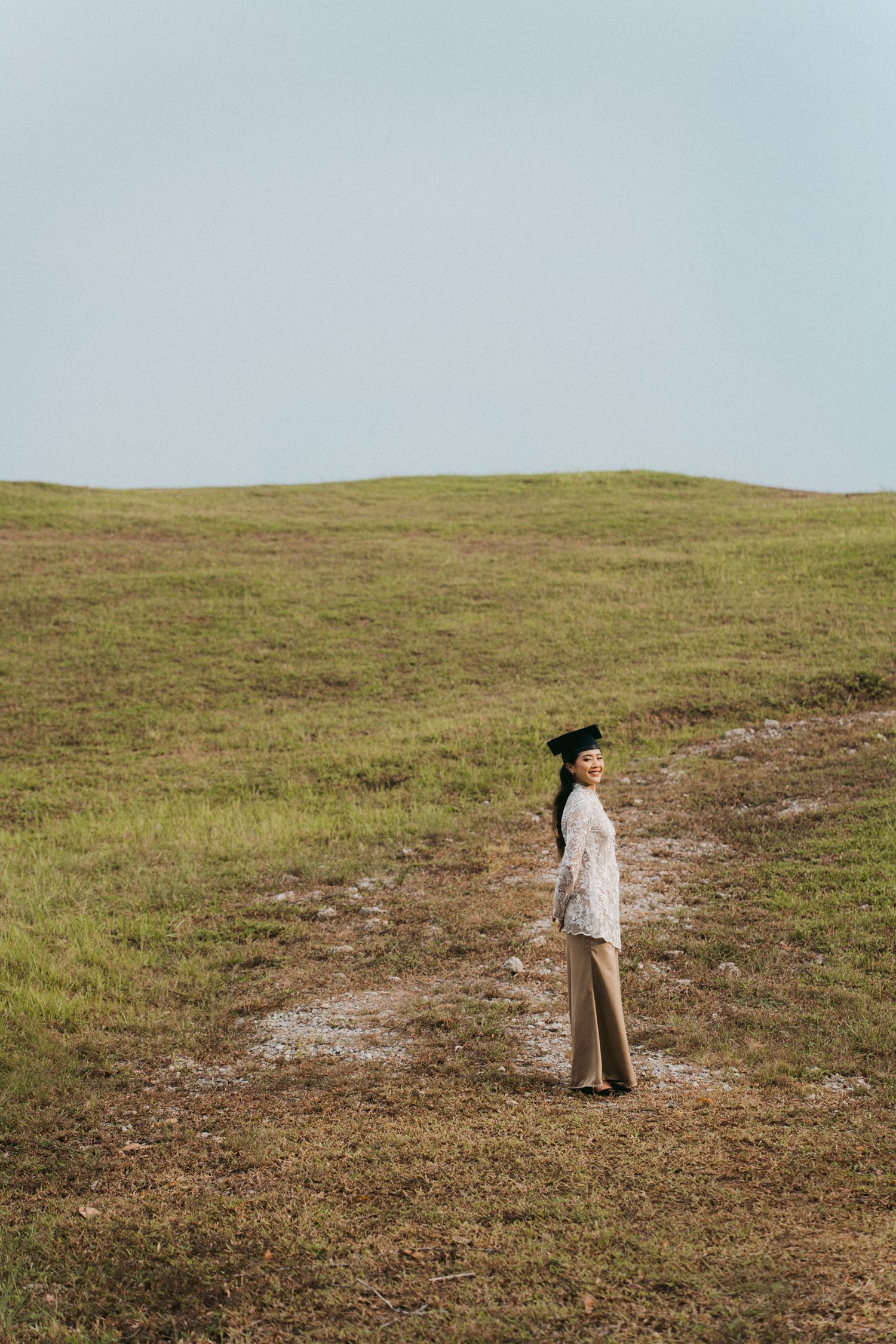A person stands in solitude on a grassy hillside path against an overcast sky.