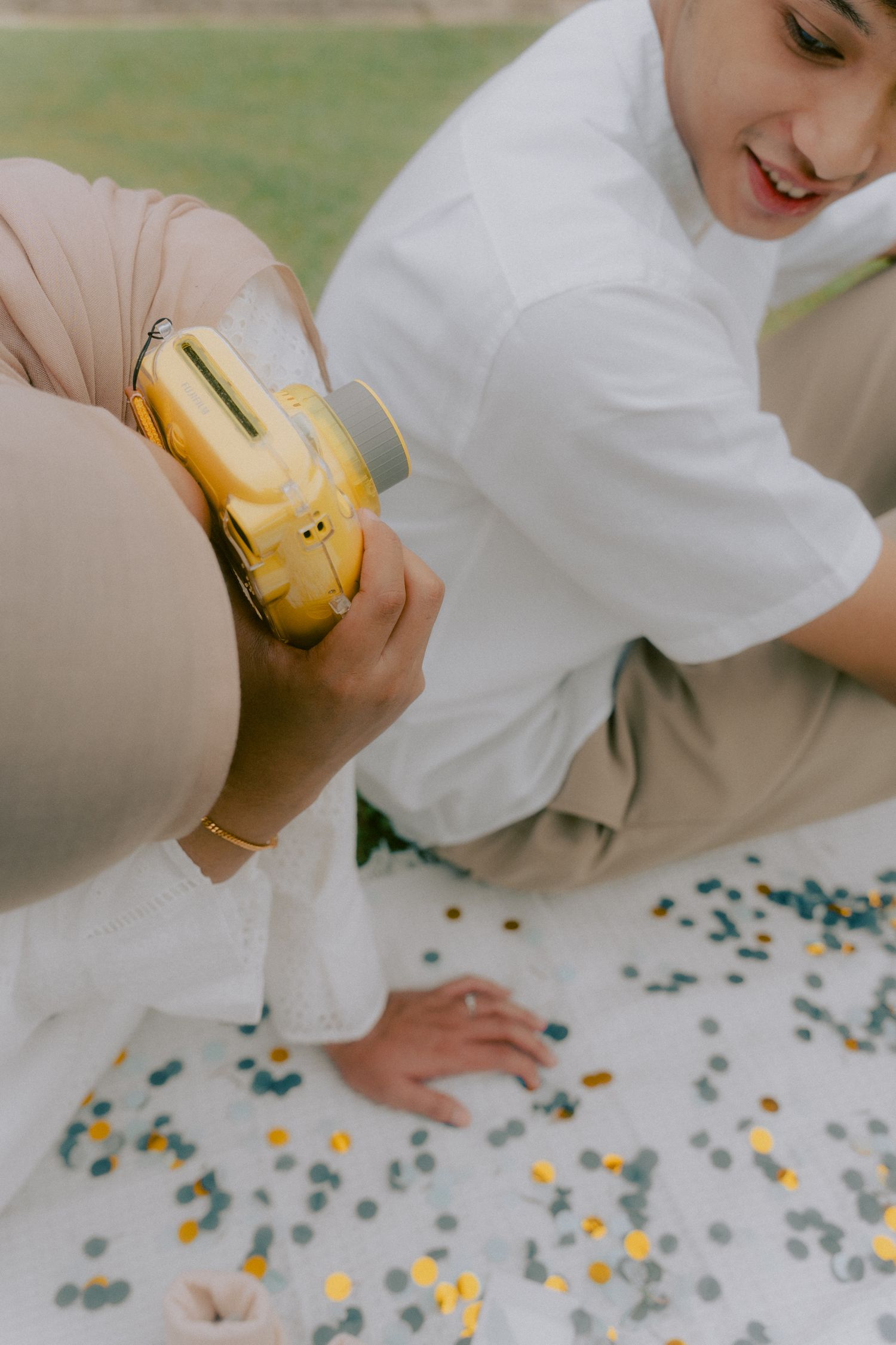 Someone holds yellow bananas while sitting on a picnic blanket decorated with colorful confetti.