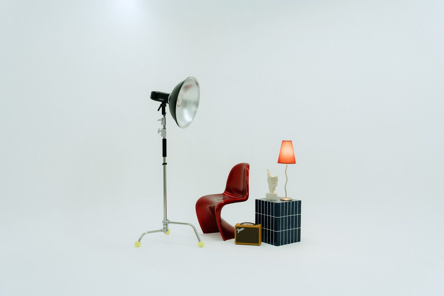 Studio setup with a red chair, small lamp on dark cube, and tall photography strobe light on white background.